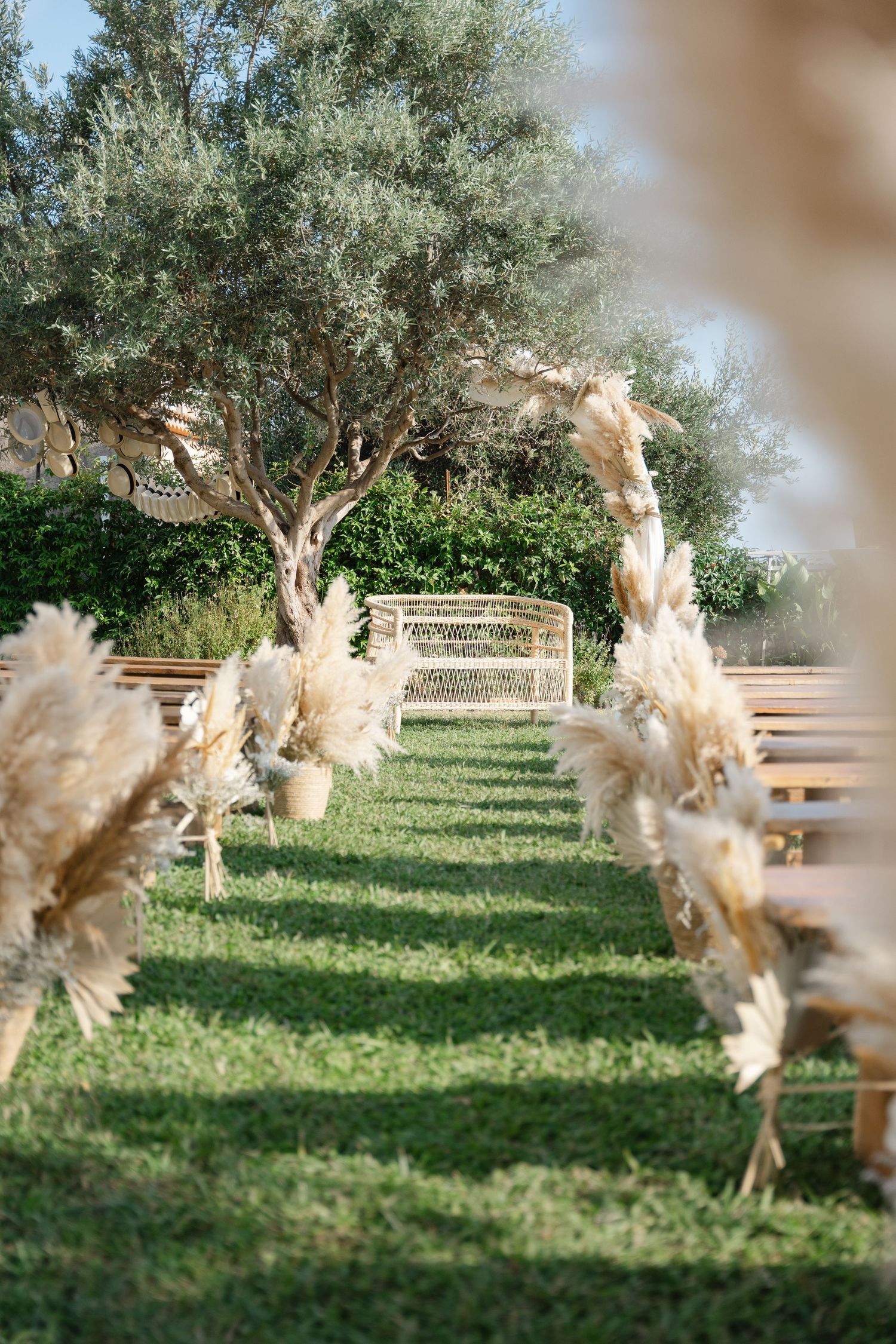 Outdoor boho wedding ceremony aisle decorated with pampas grass arrangements leading to a rattan arch.