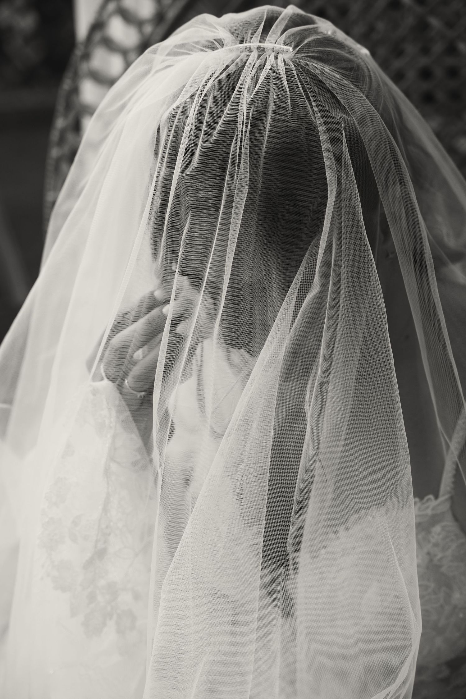 Black and white close-up of bride wearing a delicate veil covering her face at wedding.