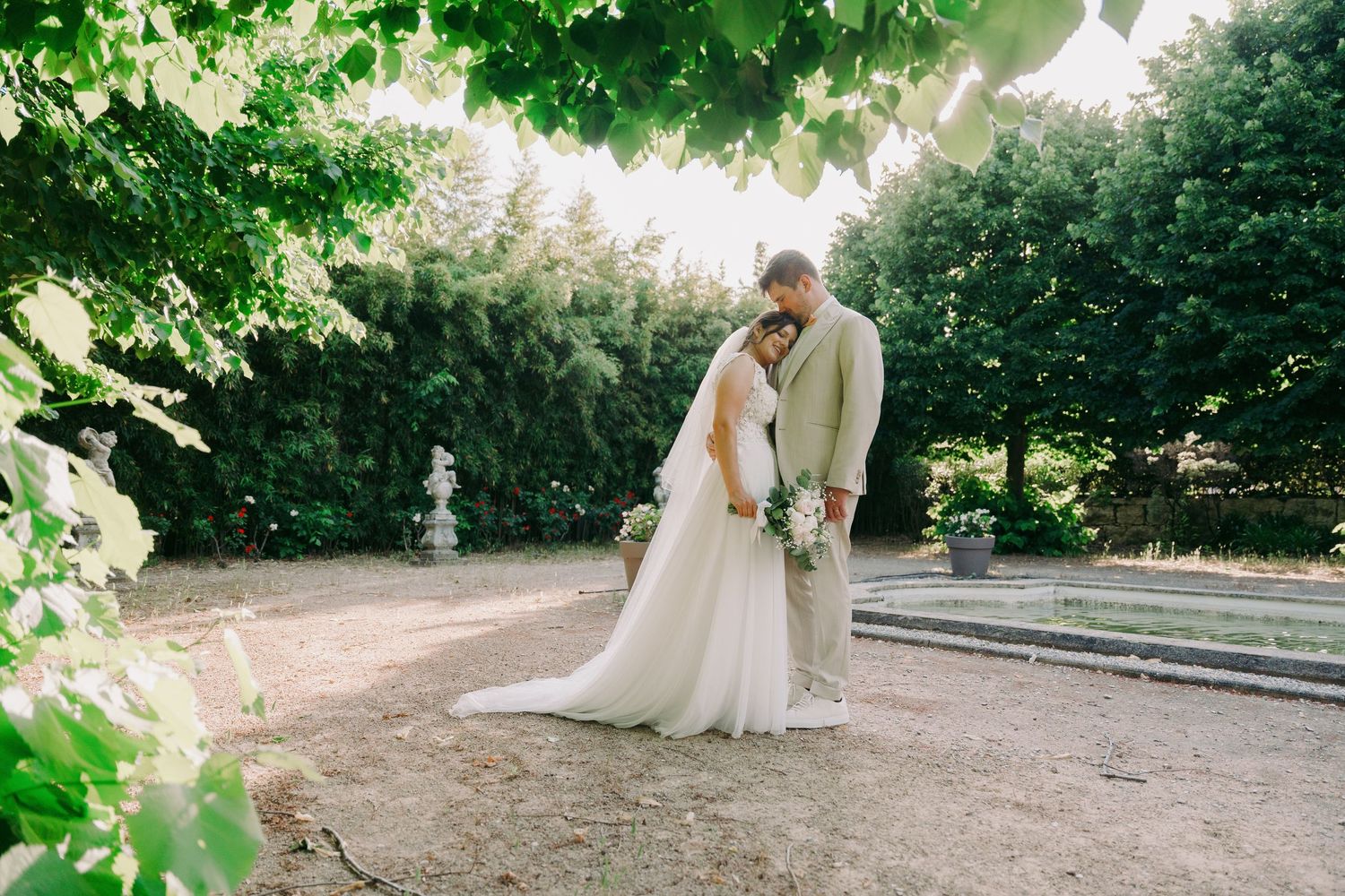 Bride and groom sharing romantic moment under lush green trees in garden wedding venue.