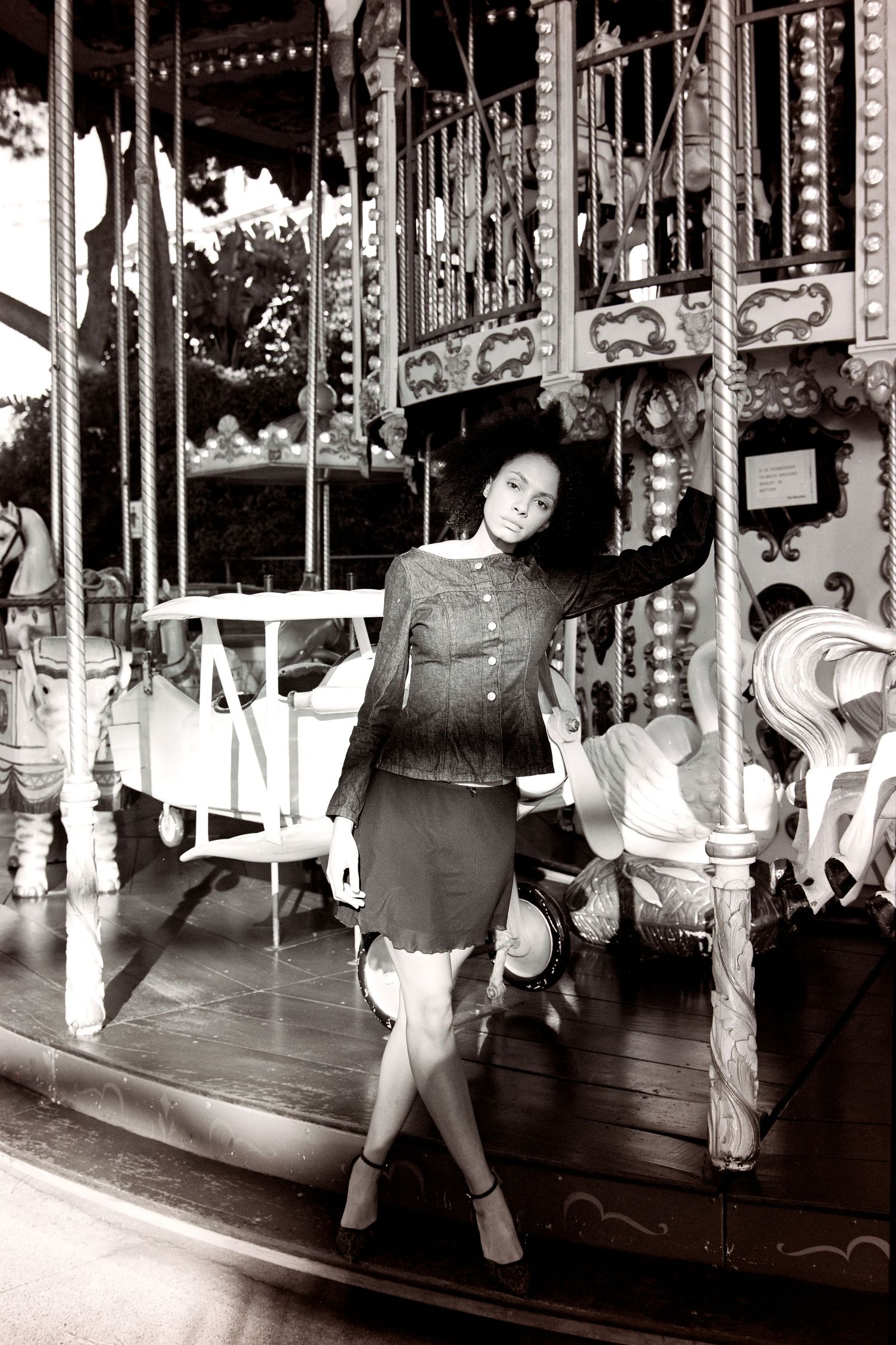 Black and white photo of woman posing on vintage carousel at amusement park.