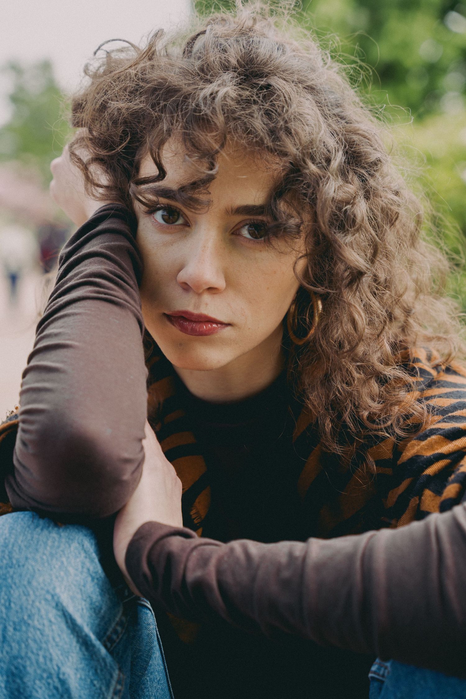 Close-up portrait of curly-haired woman in tiger-print top with gold hoop earrings outdoors.