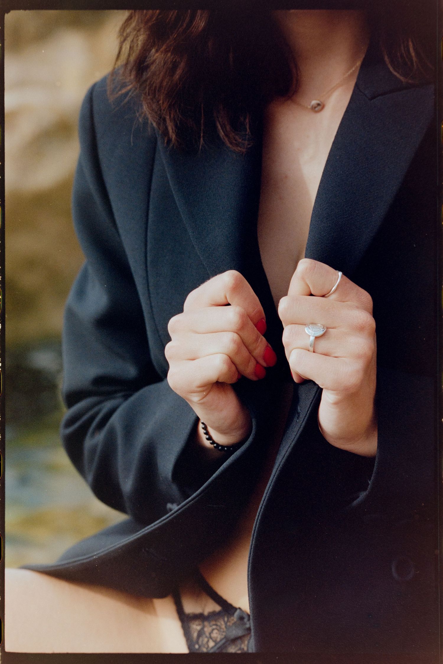 Close-up of woman in black blazer holding lapels, wearing ring and delicate necklace.