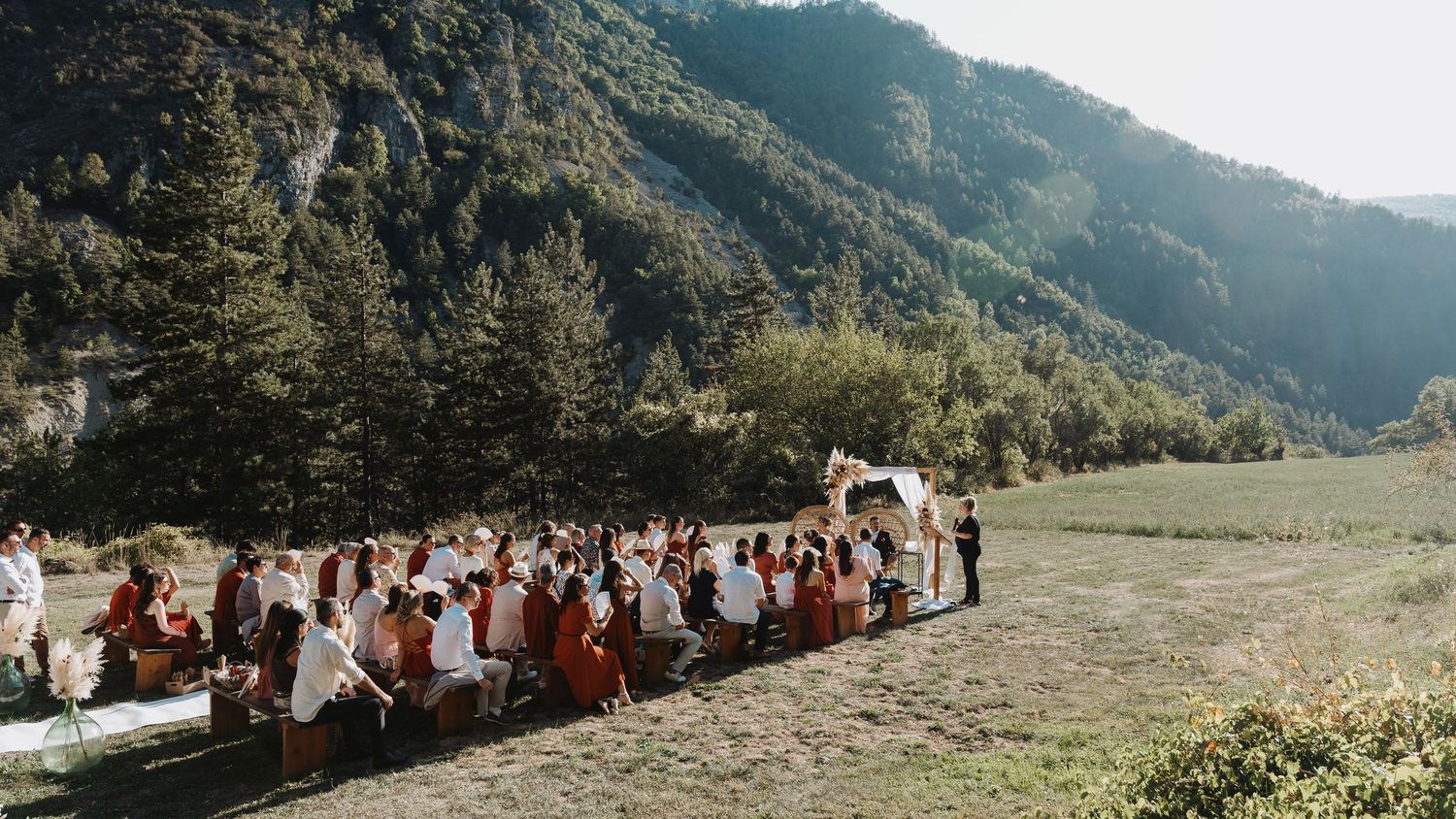 Outdoor wedding ceremony with guests seated in mountain valley surrounded by lush green landscape.