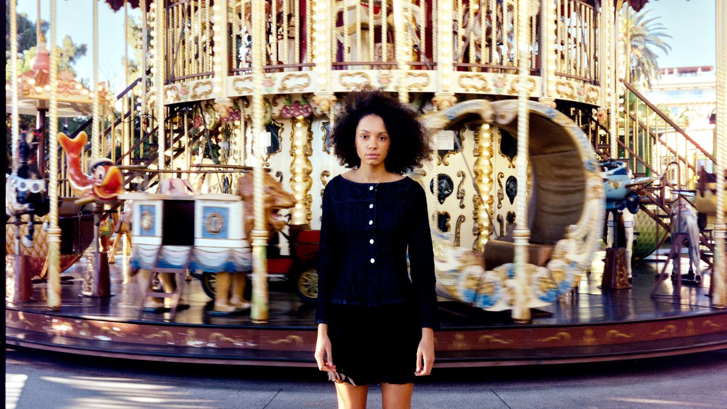 Woman in black dress standing before spinning carousel with motion blur background.