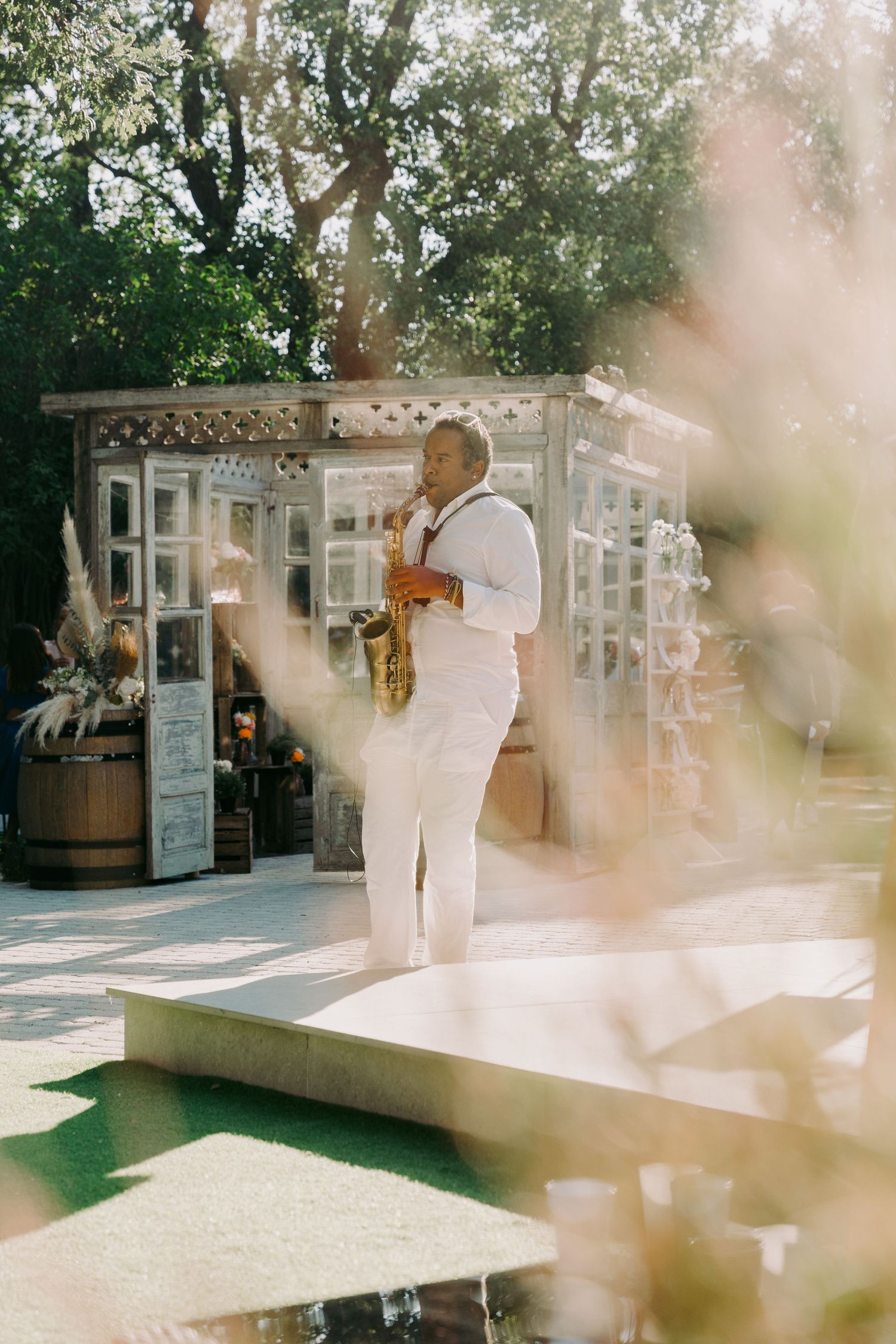 Saxophonist in white suit performing outdoors at a wedding reception in a garden venue.
