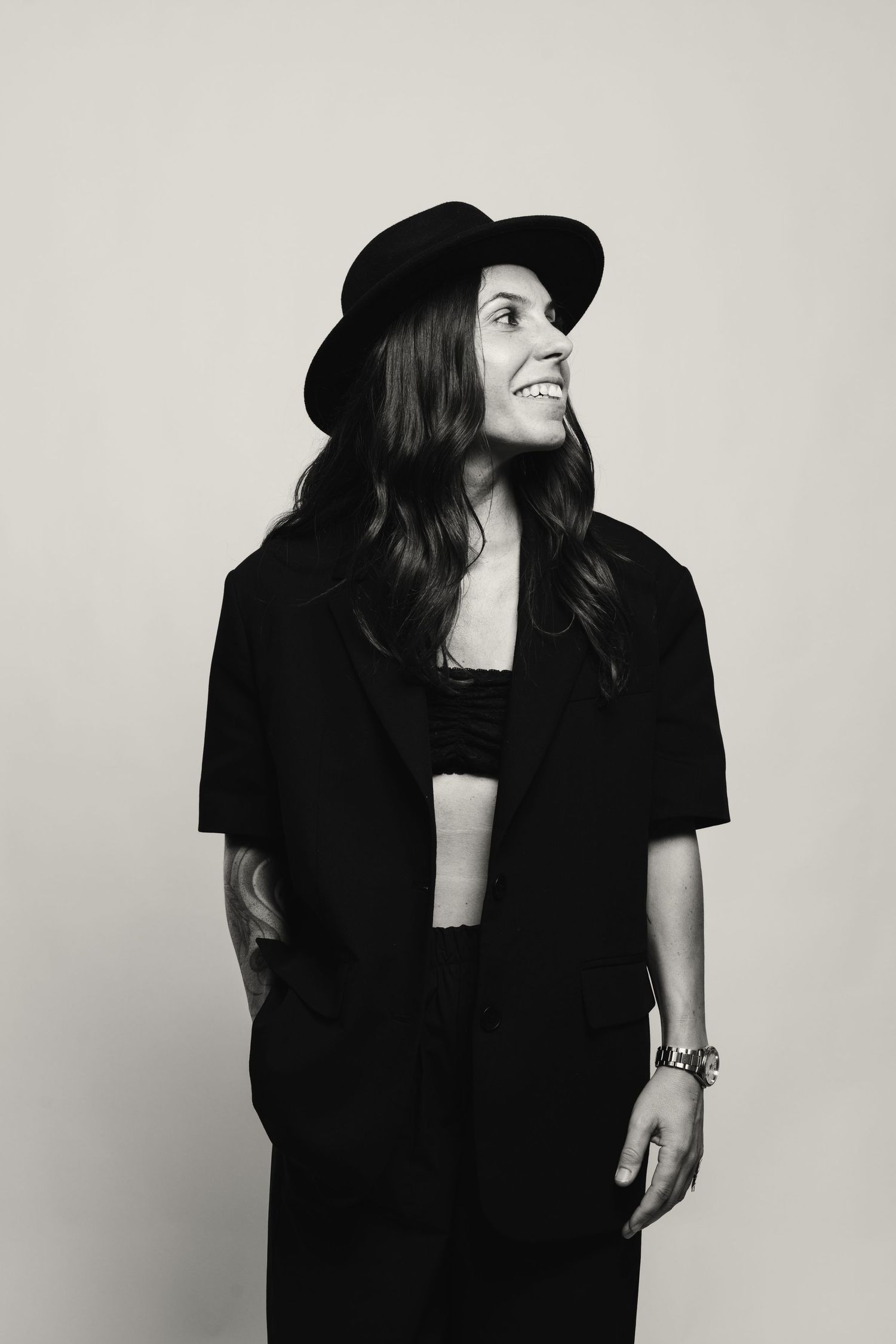 Smiling woman in black hat and suit posing in black and white studio photo.