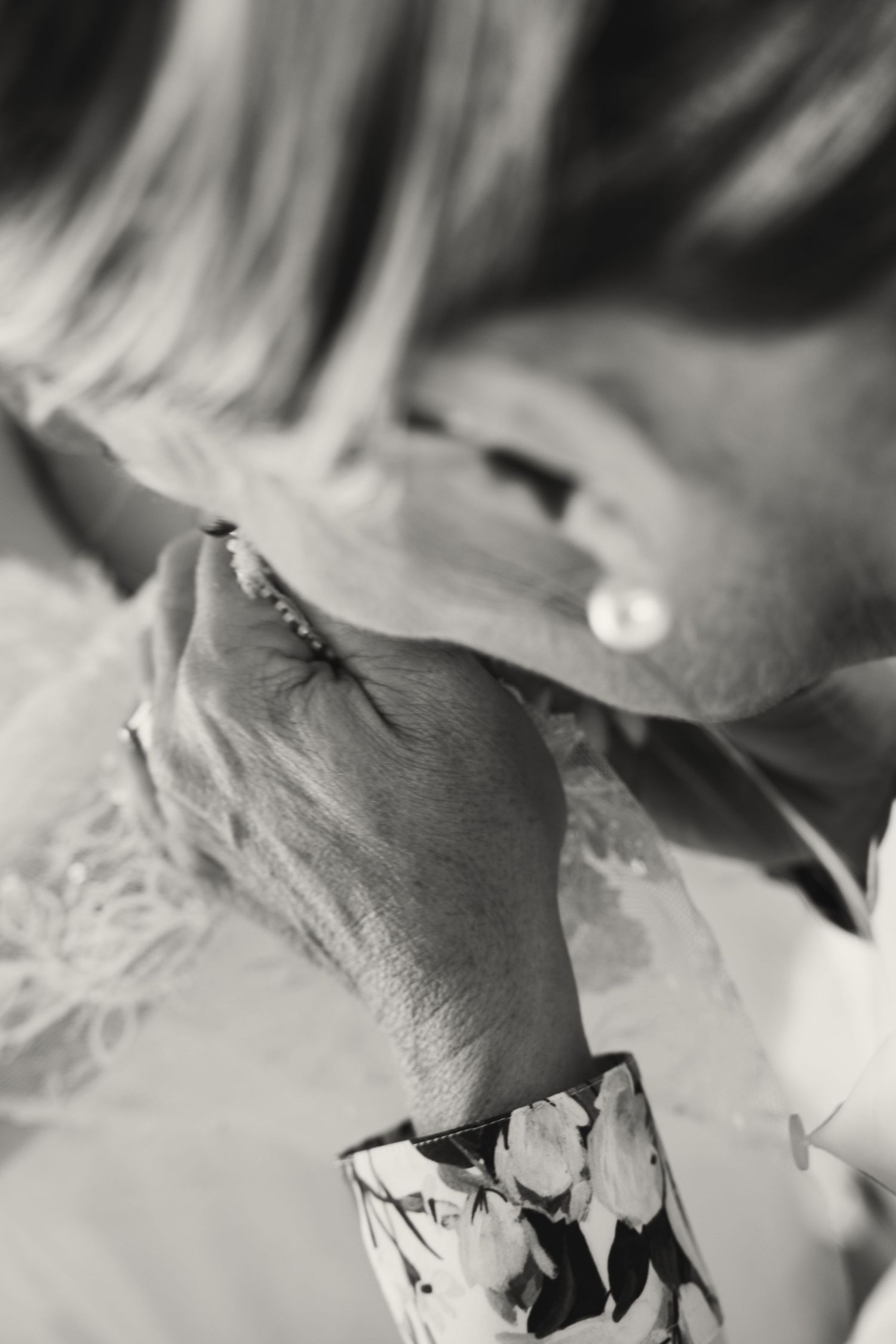 Close-up black and white detail of an elderly hand holding a bride's lace-adorned wrist.