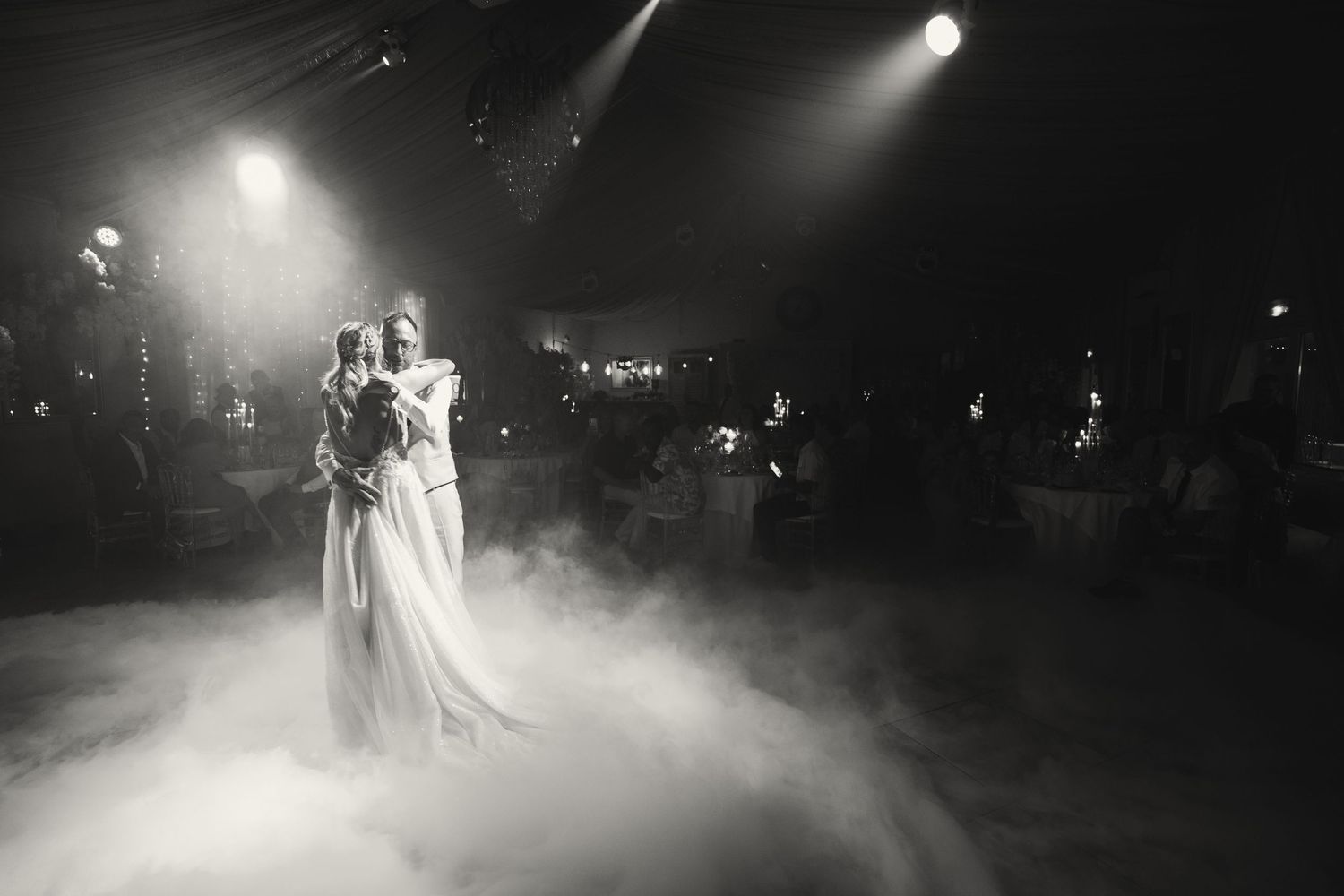 Black and white photo of a couple sharing their first dance on a foggy, dramatically lit wedding reception dance floor.