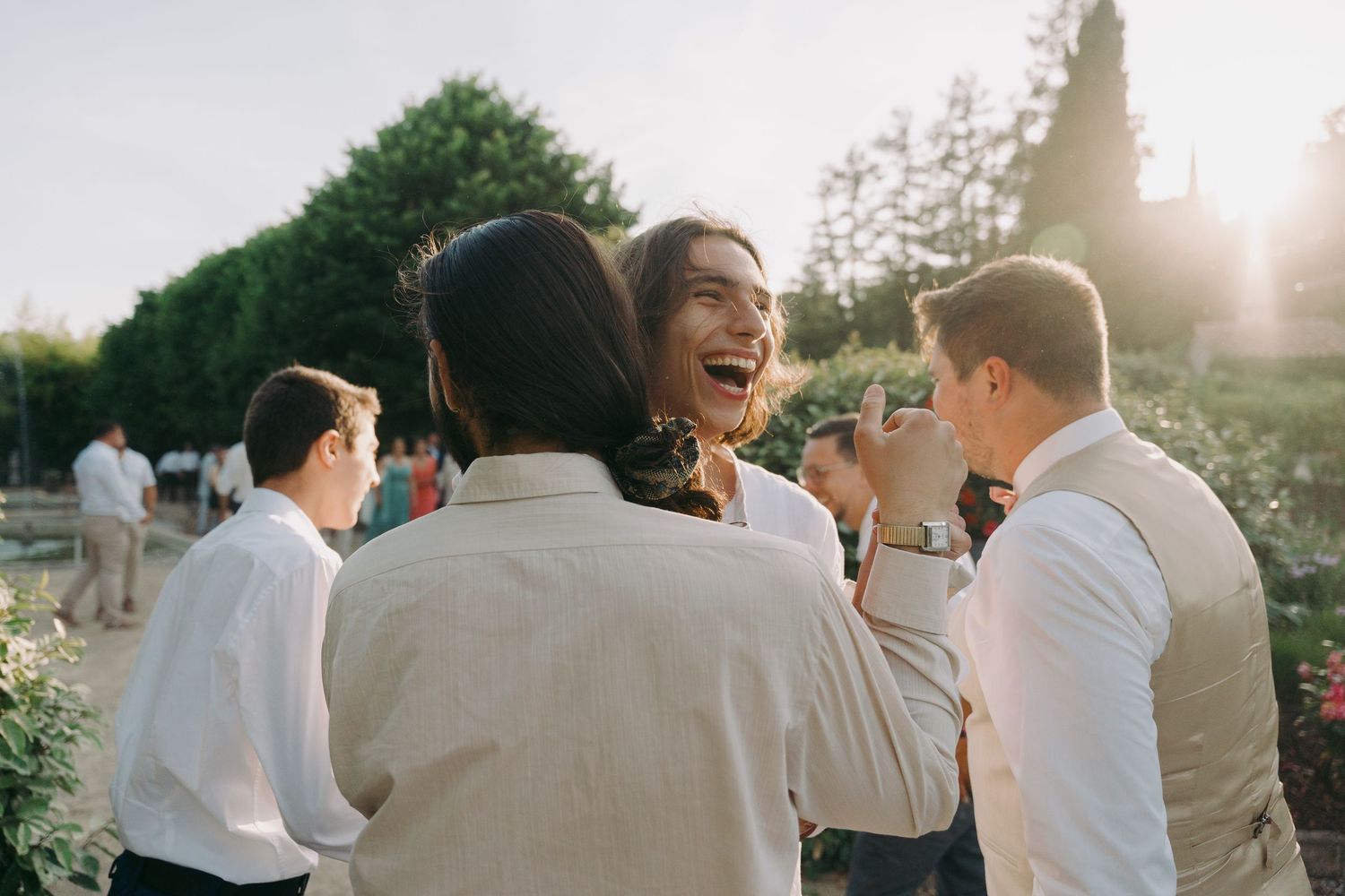 Joyful wedding guest laughing with friends during golden hour outdoor reception celebration.