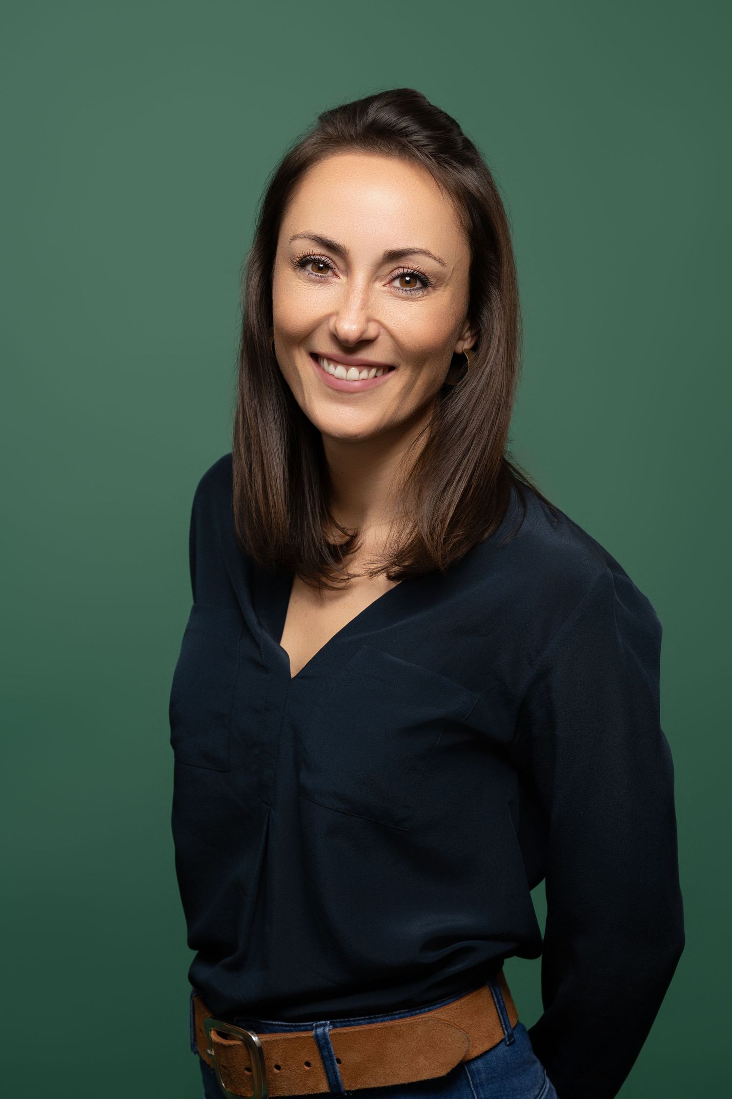 Professional woman in navy blouse smiling against green background, business portrait.