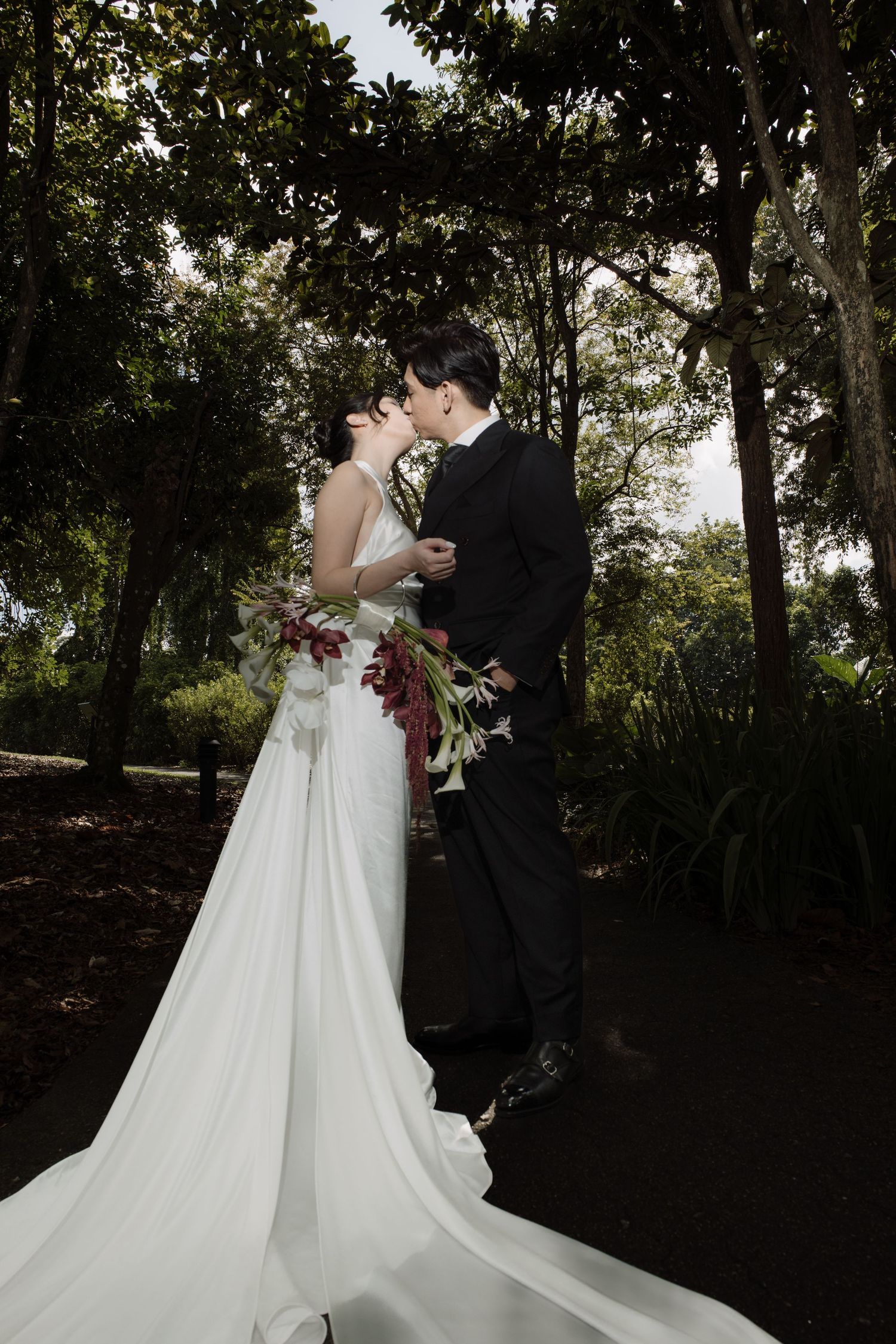 Bride and groom share a romantic kiss in a lush garden, bride holding a bouquet in a flowing white gown.