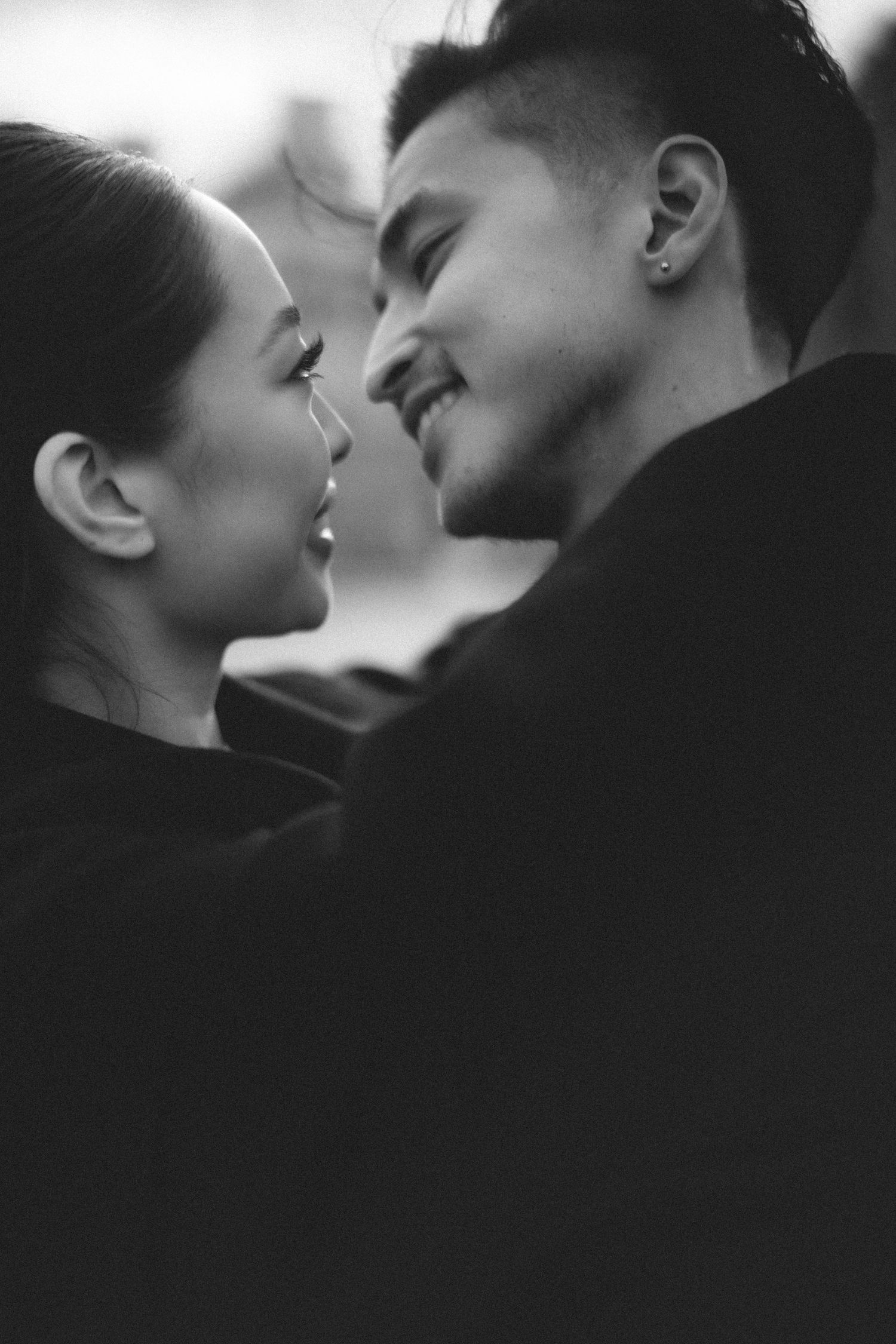 Black and white photo of a romantic couple smiling and leaning in close together, almost kissing.