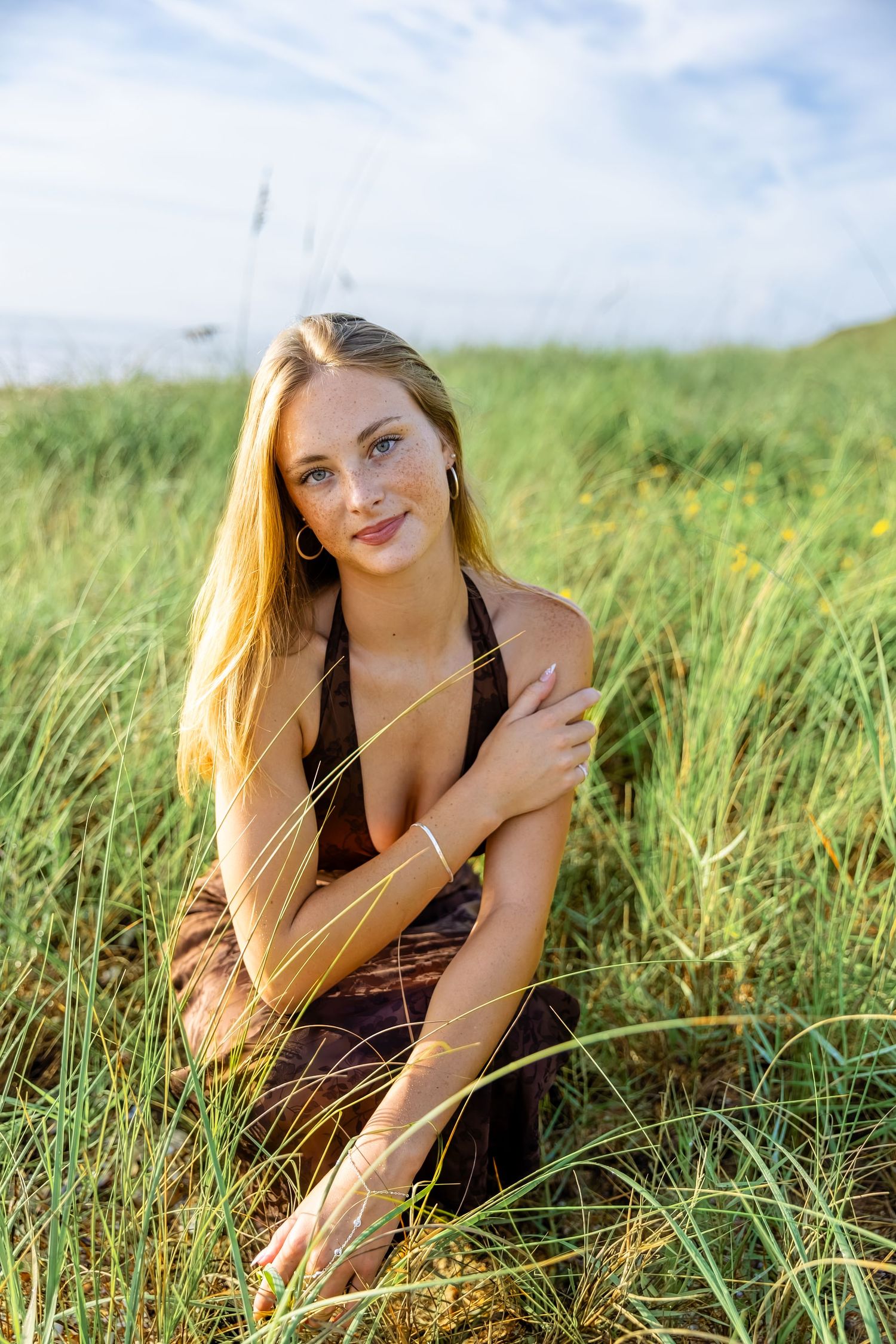 Senior girl sitting in tall grass on Guana Reserve Middle Beach smiling during sunset.