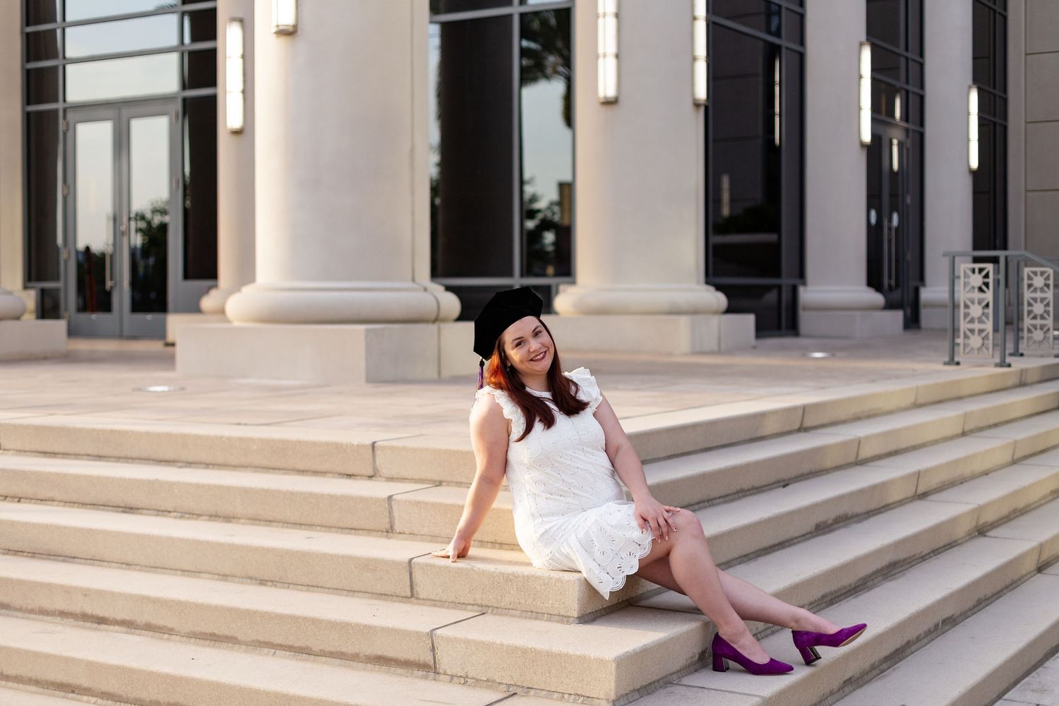 Graduate woman sitting on Duval County Courthouse steps outside during golden hour.