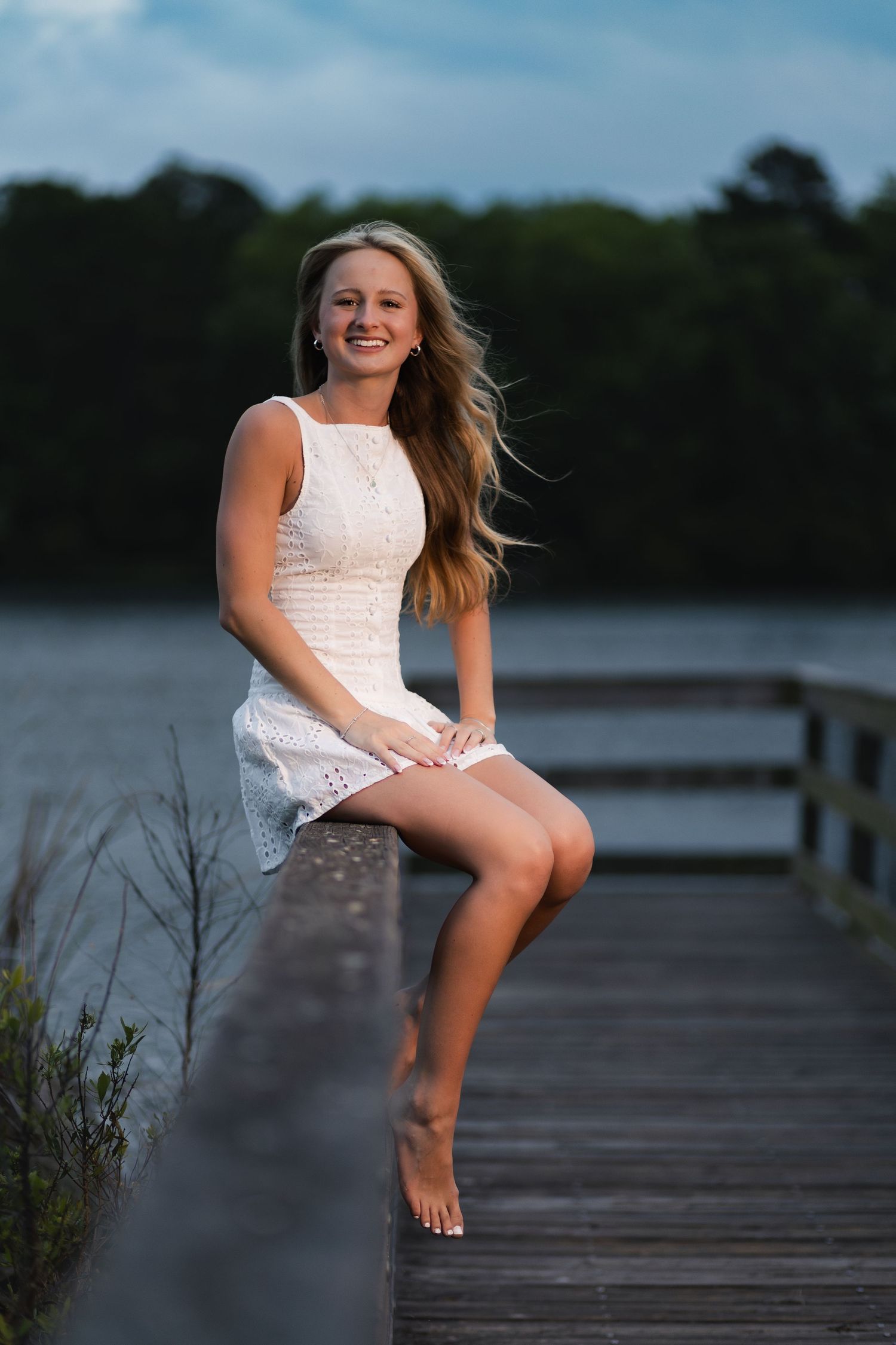 Senior girl in a white romper posing on a dock during her senior session in Jacksonville, Florida.