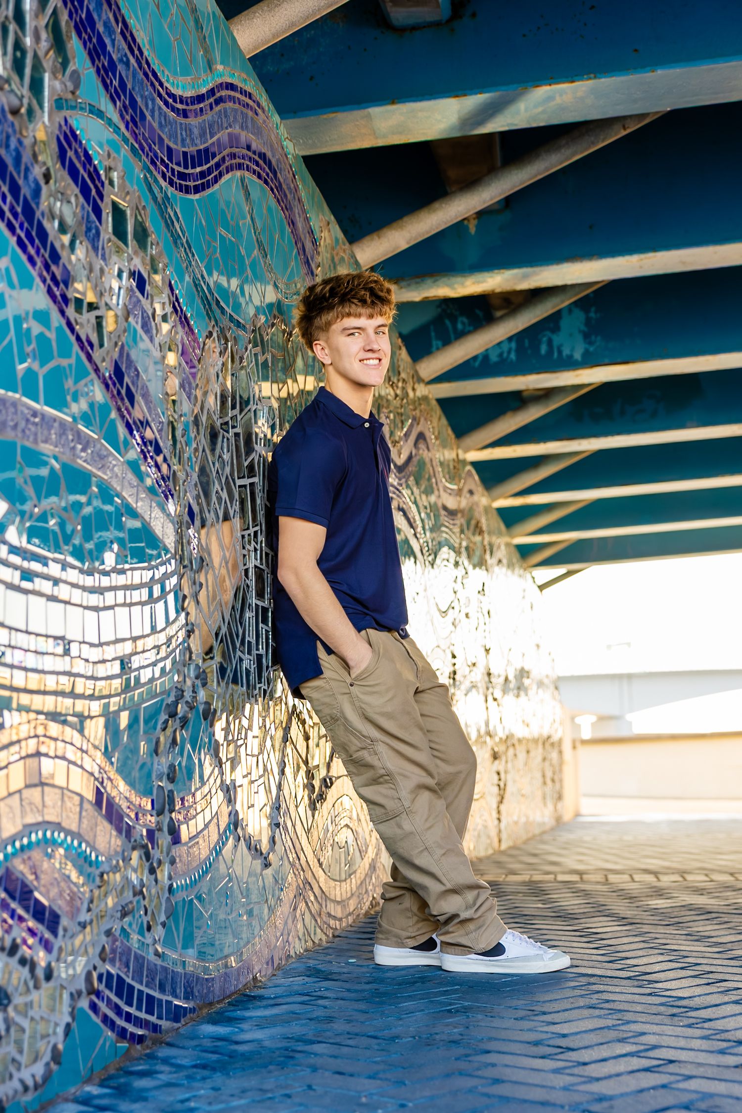 Senior guy sits against a colorful mosaic wall under a concrete bridge structure on the Southbank Riverwalk.