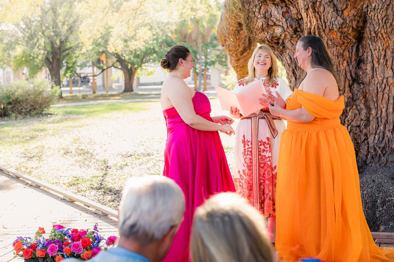 Two brides in pink and orange gowns exchange vows at Treaty Oak Park.