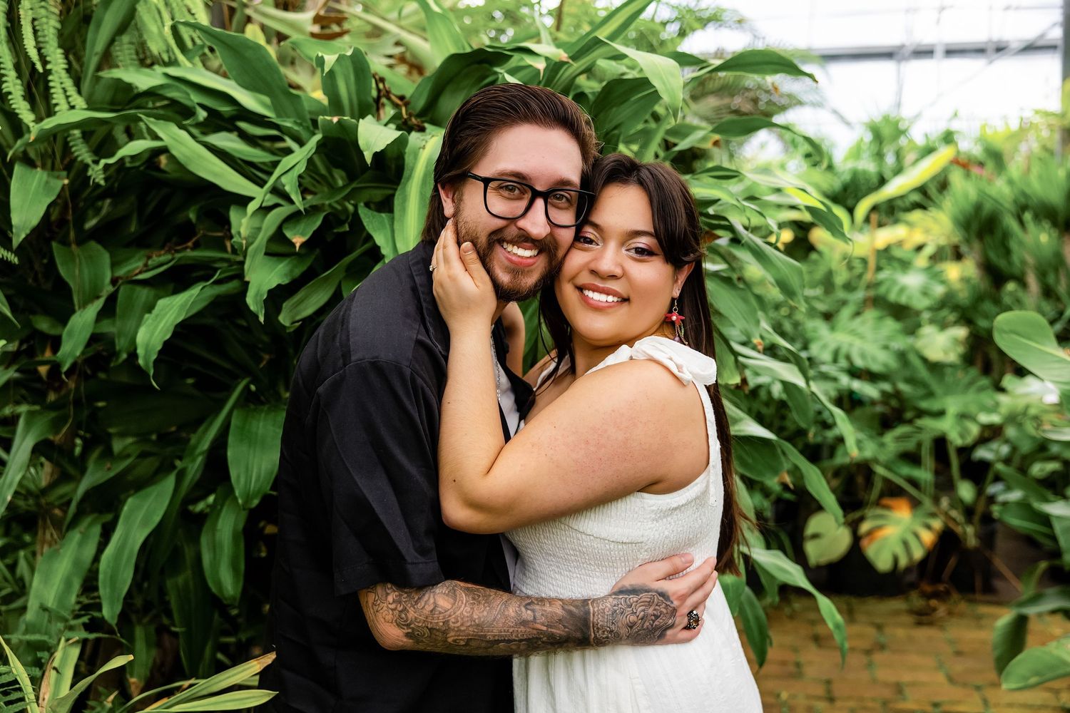Happy couple embracing during engagement session in a lush greenhouse in St. Augustine.