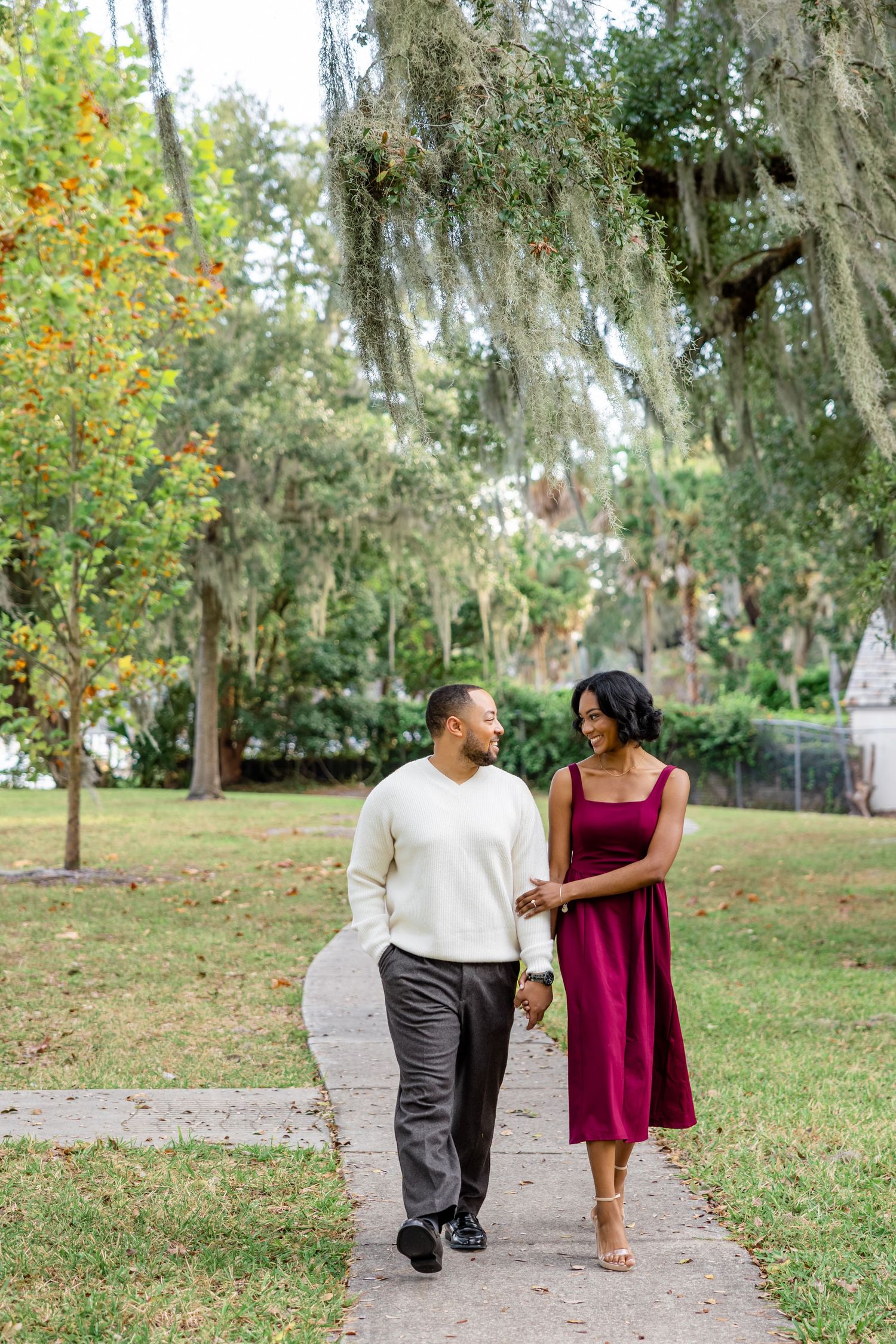 Man proposes to woman couple walks hand-in-hand on a path beneath Spanish moss-draped trees at Stockton Park.