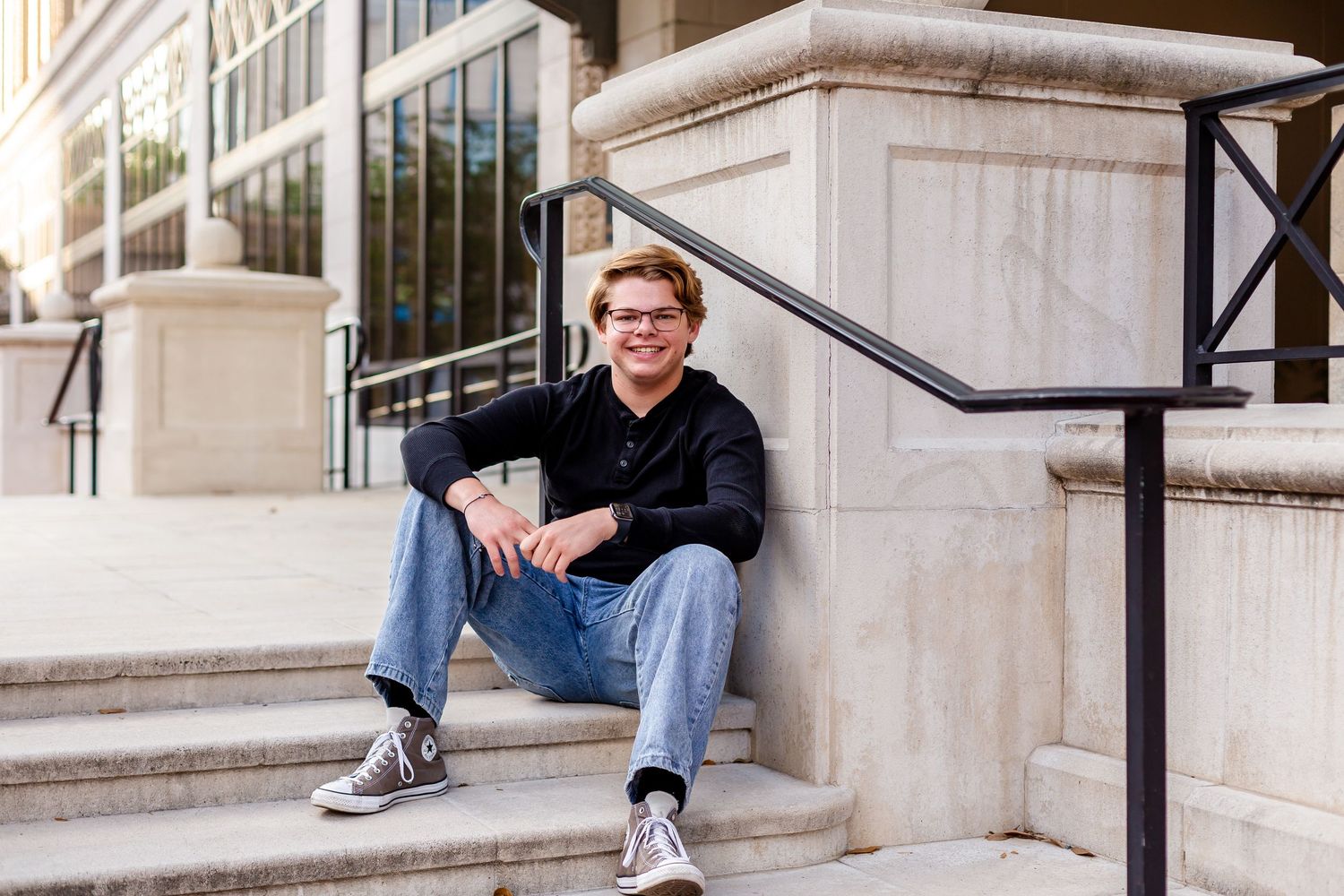 Senior boy sitting on the outdoor steps of the Jacksonville City Hall building smiling for senior portraits.