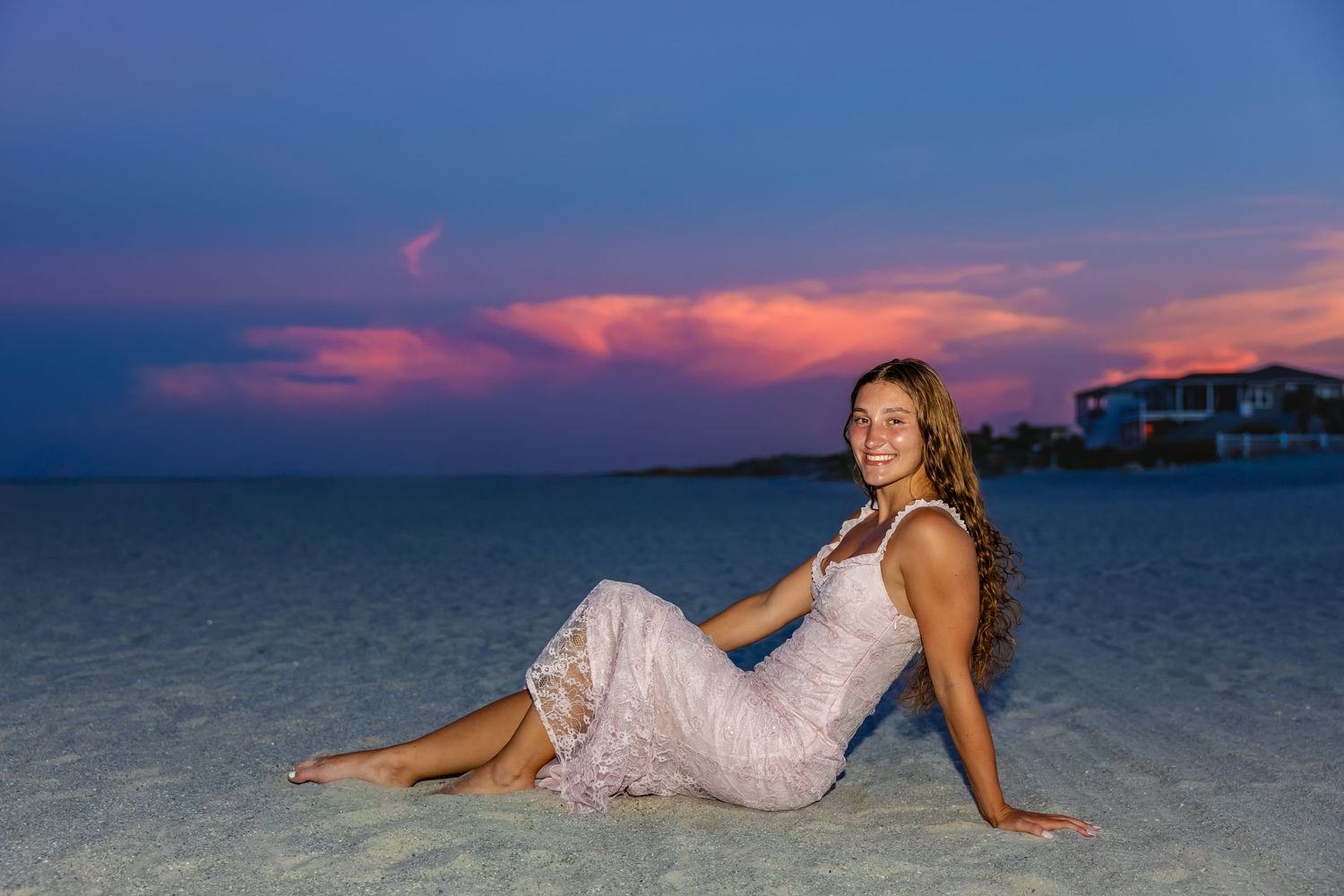 Senior girl sitting on St. Augustine beach with a colorful pink and purple sunset.