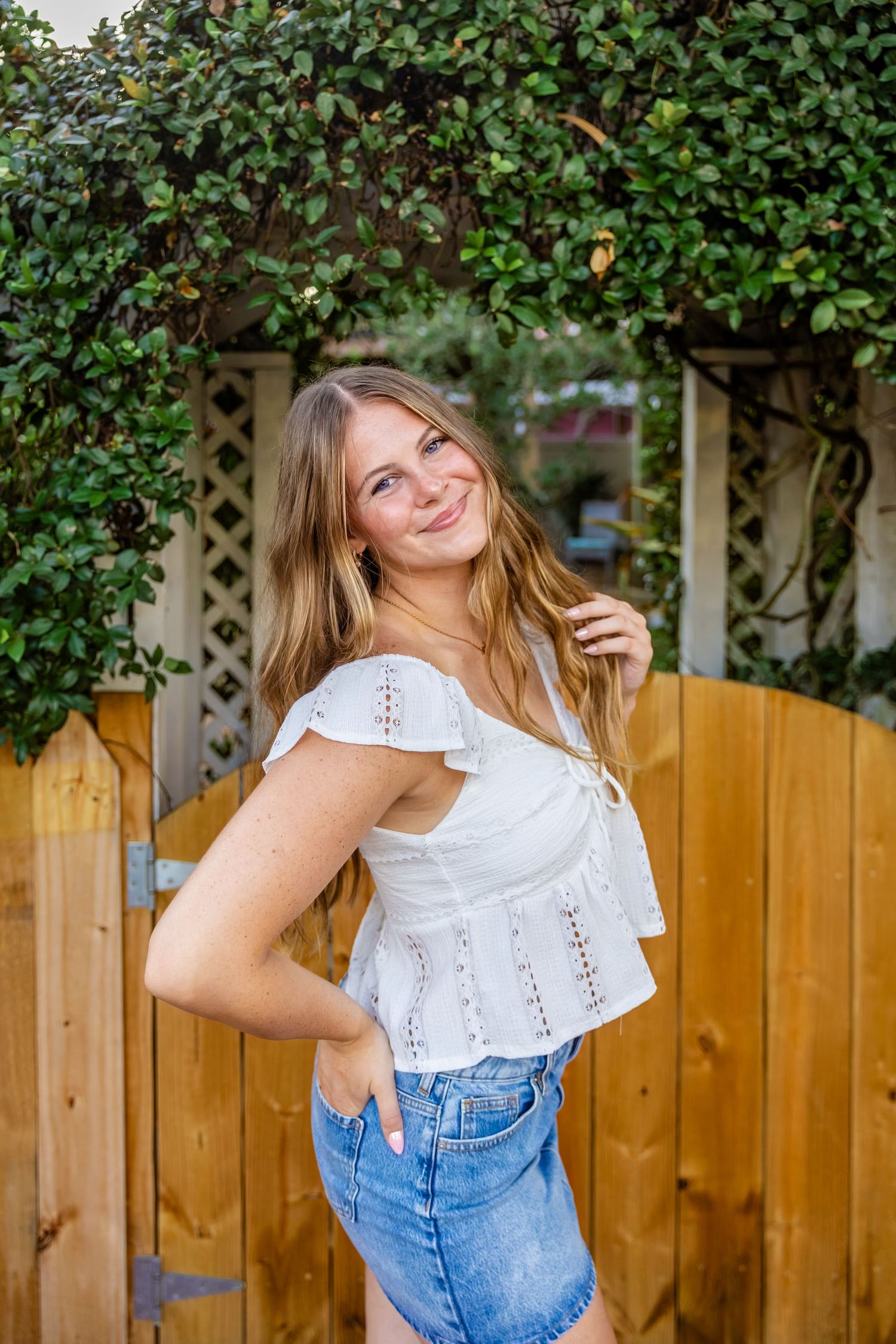 Senior girl smiling on sidewalk near wooden gate in Jacksonville Beach.