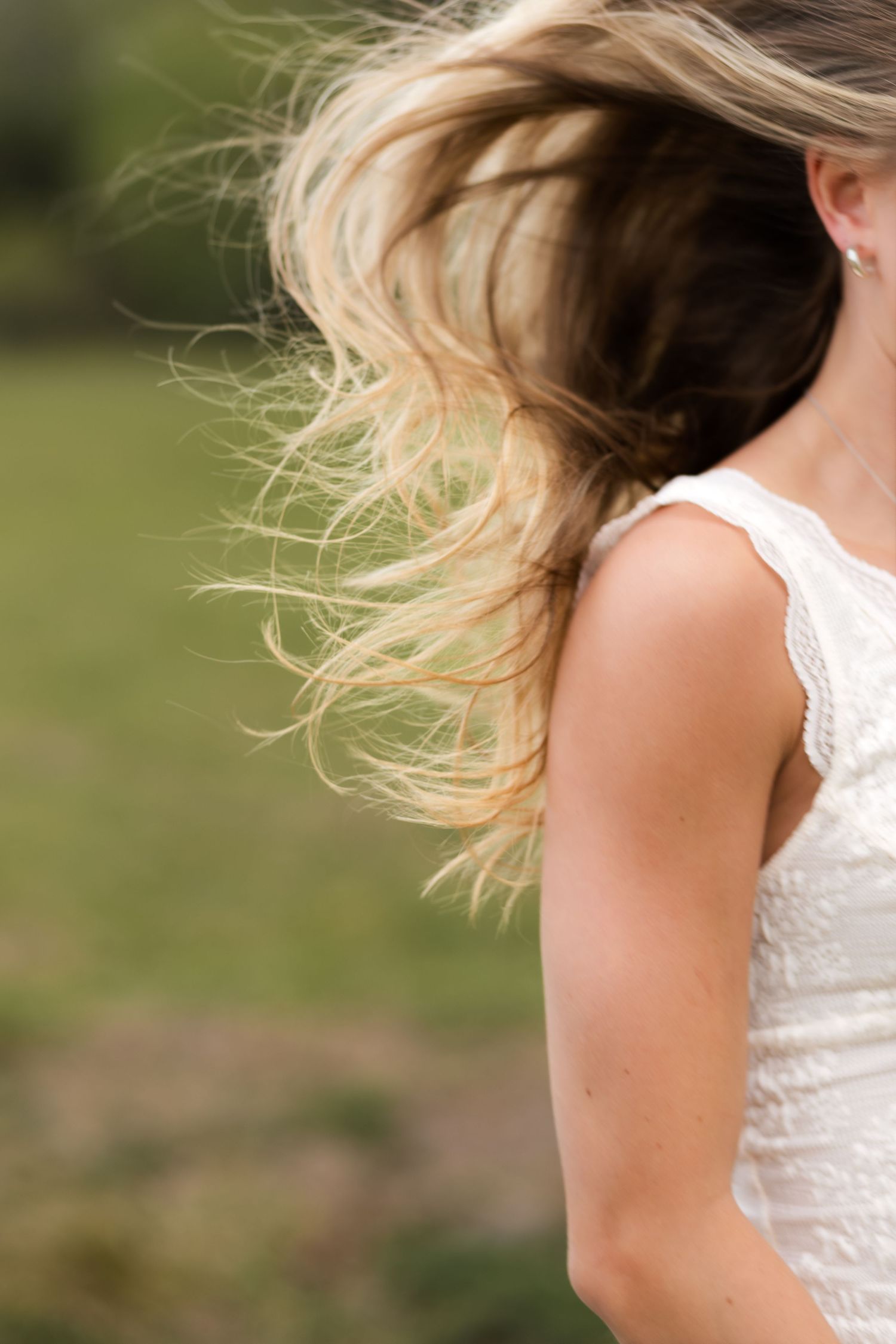 Blonde woman in white lace dress with hair flowing in the wind outdoors.