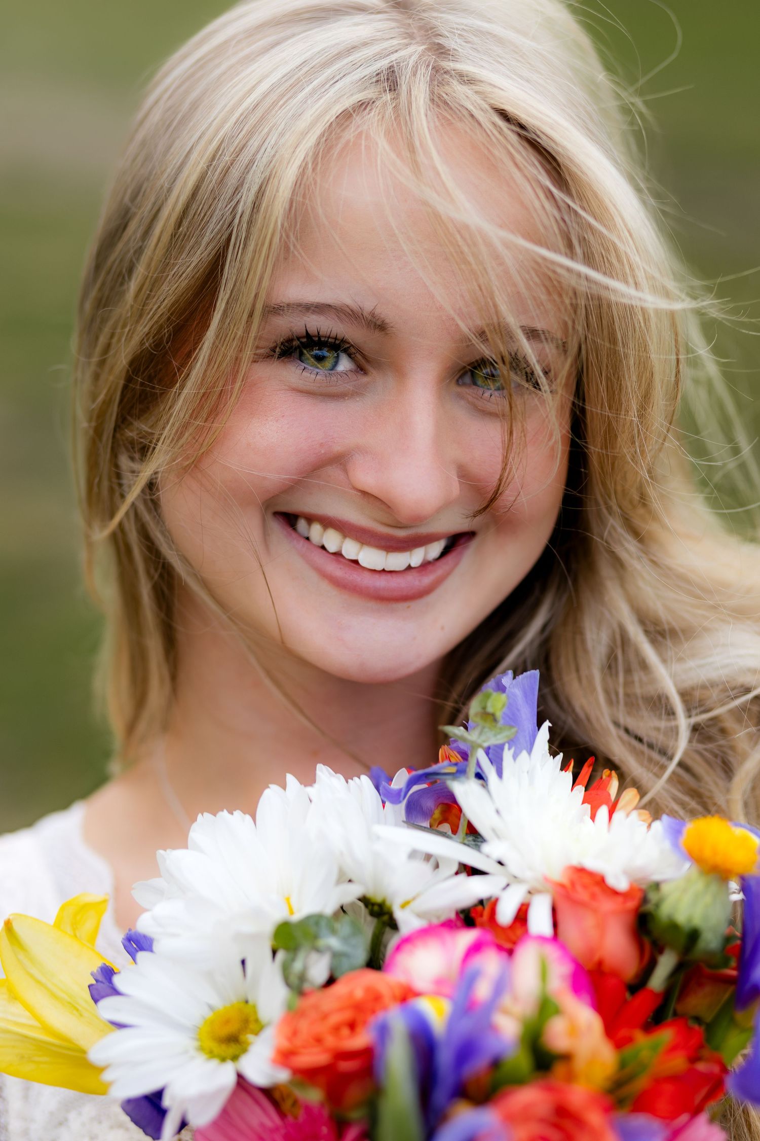 Smiling young blonde woman holding a colorful bouquet of mixed flowers outdoors.