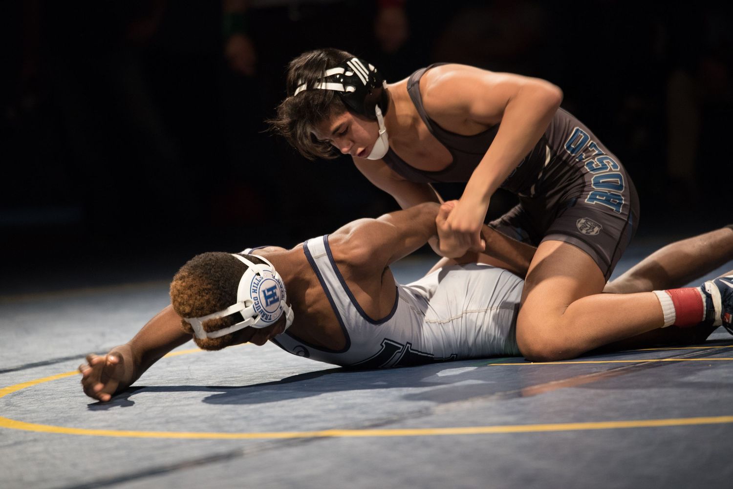 Two wrestlers compete on mat, one pinning the other in intense match.