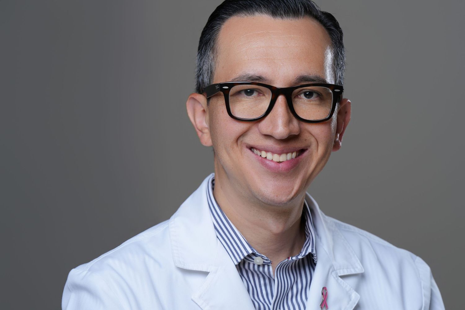 Smiling male doctor in white lab coat and black glasses posing for professional headshot.