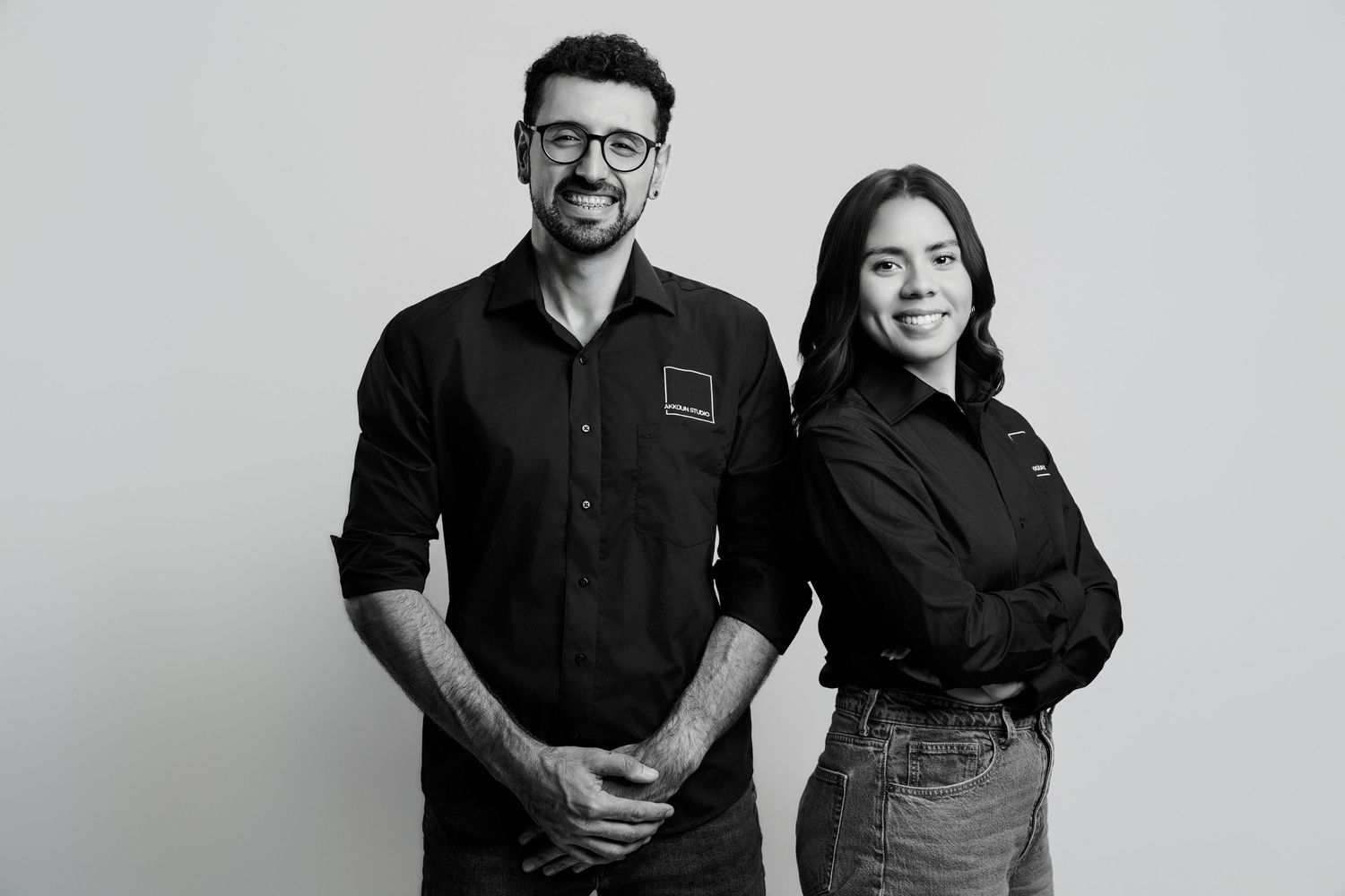 Black and white portrait of a man and woman in black uniforms smiling against a light background.