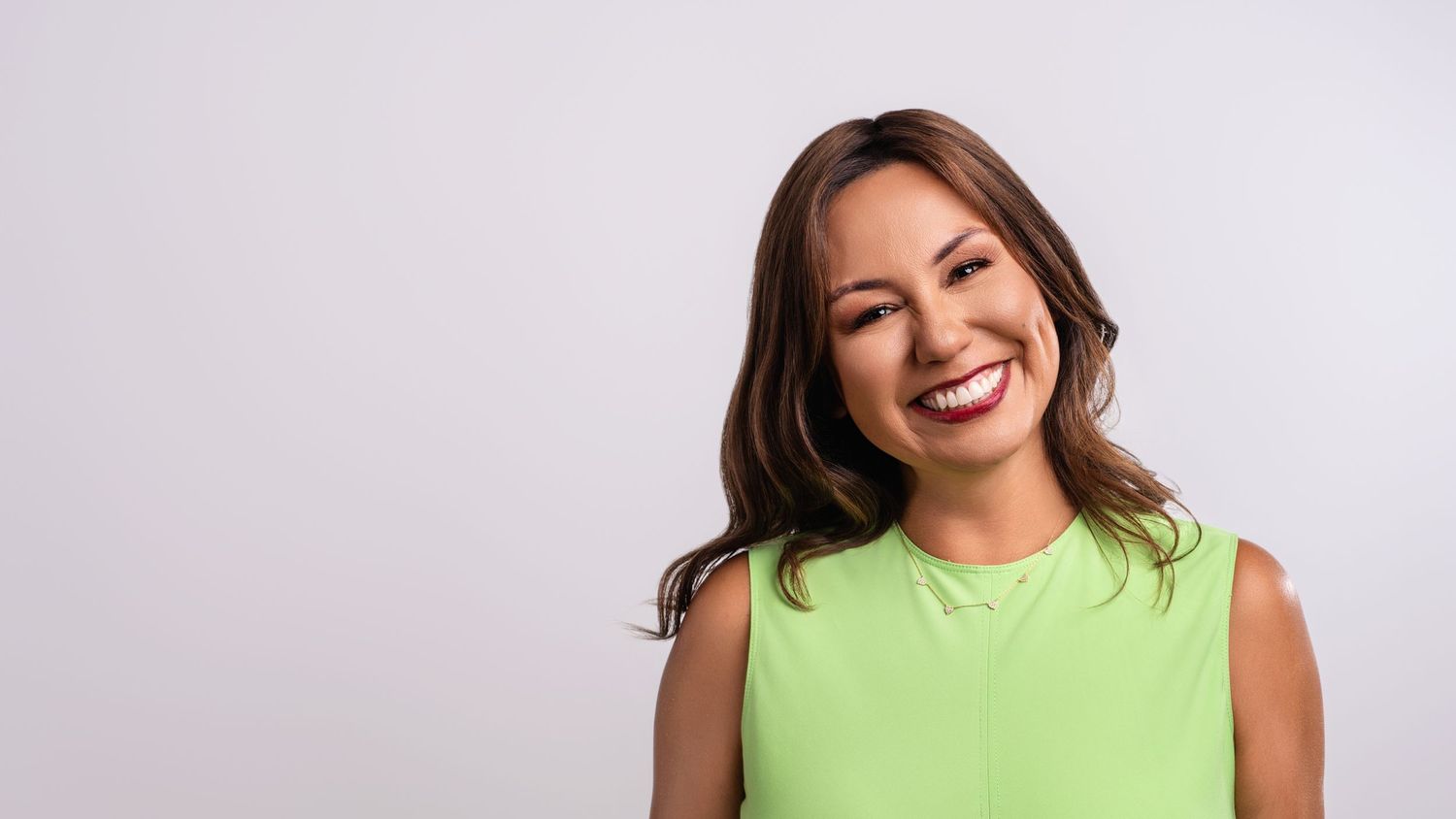 Cheerful brunette woman in a lime green top smiles brightly in a professional studio portrait.
