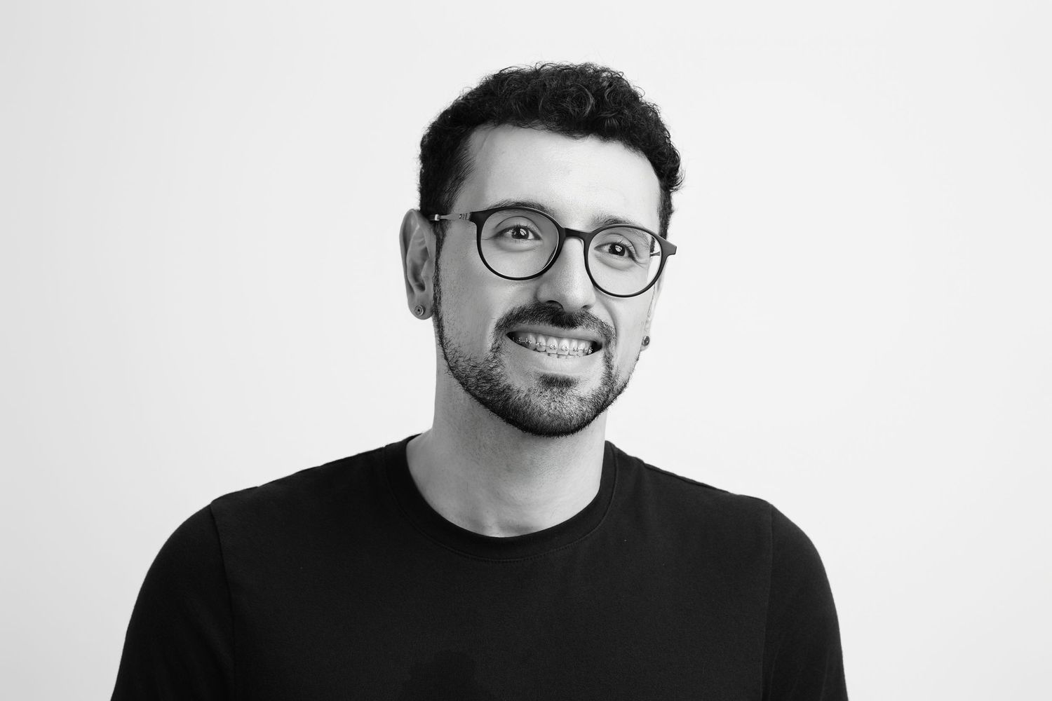Smiling man with glasses and black t-shirt in black and white professional headshot photo.