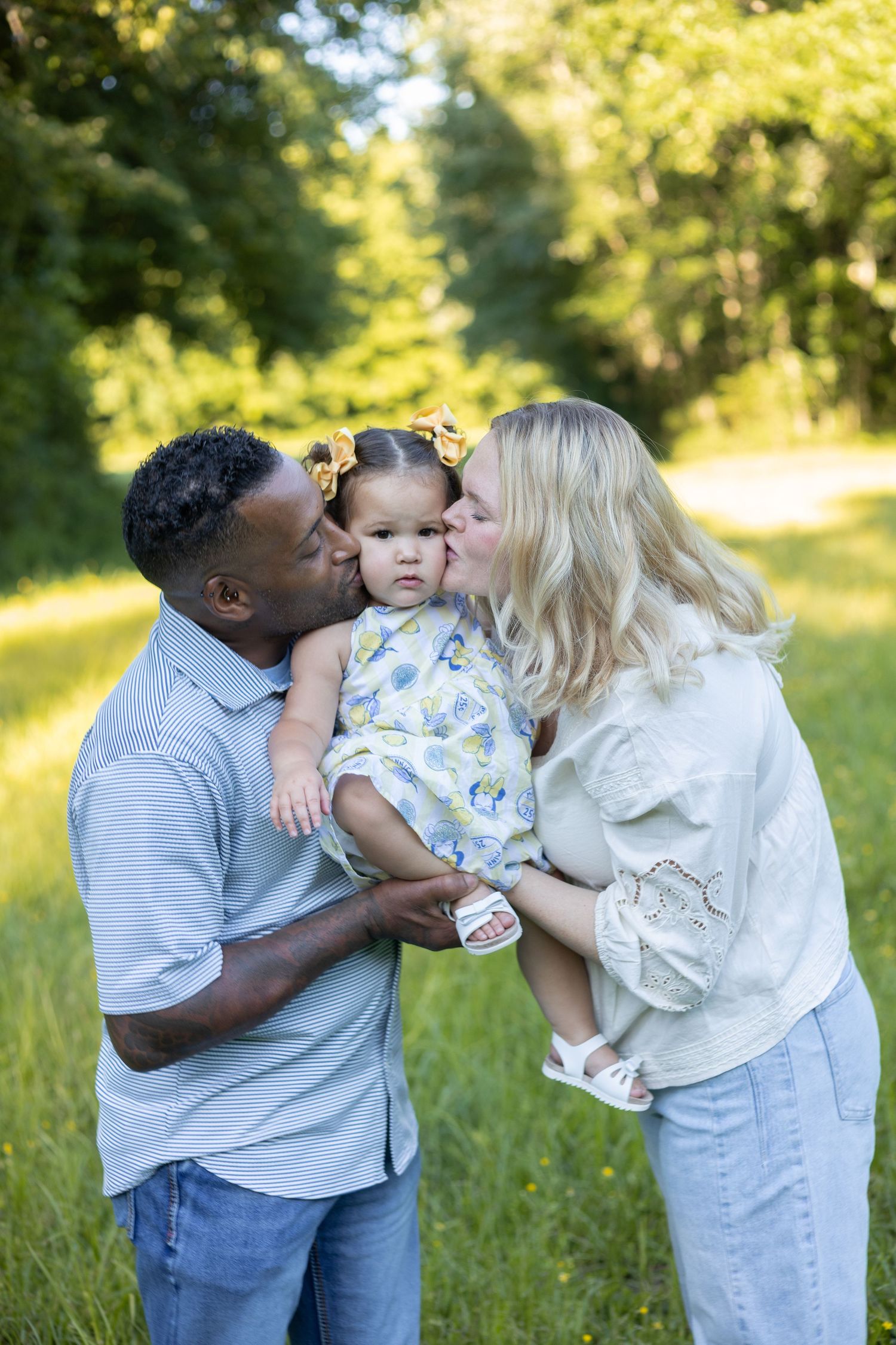 Parents kissing their toddler outdoors in a sunny field, Huntsville Alabama family session