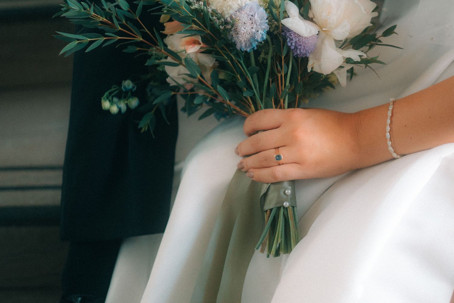 Close-up detail of a bride's hands holding a white and green floral bouquet with an engagement ring visible, wedding detail photography