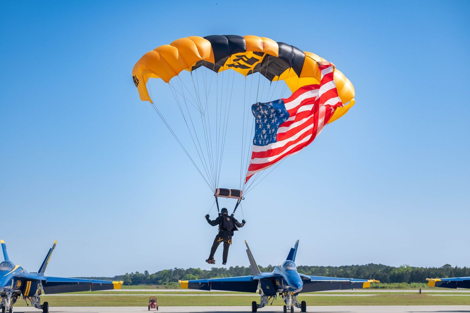 Skydiver landing with an American flag under a gold and black parachute at an airshow.