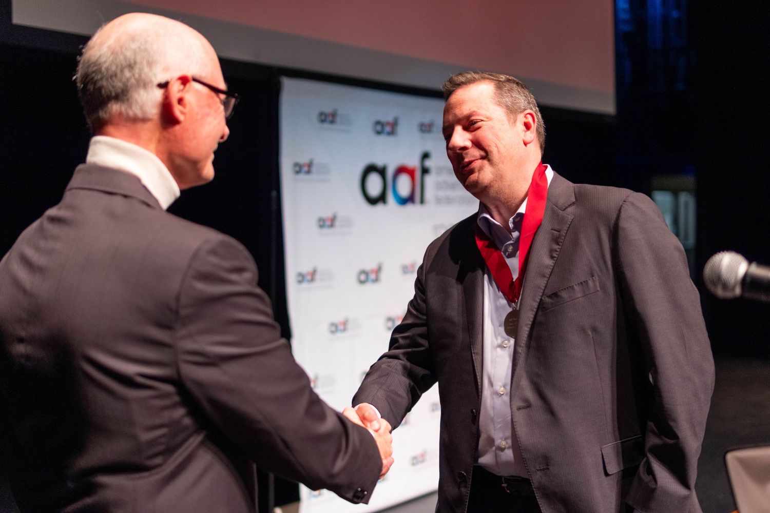 Two men in suits shake hands at AAF American Advertising Federation awards ceremony.