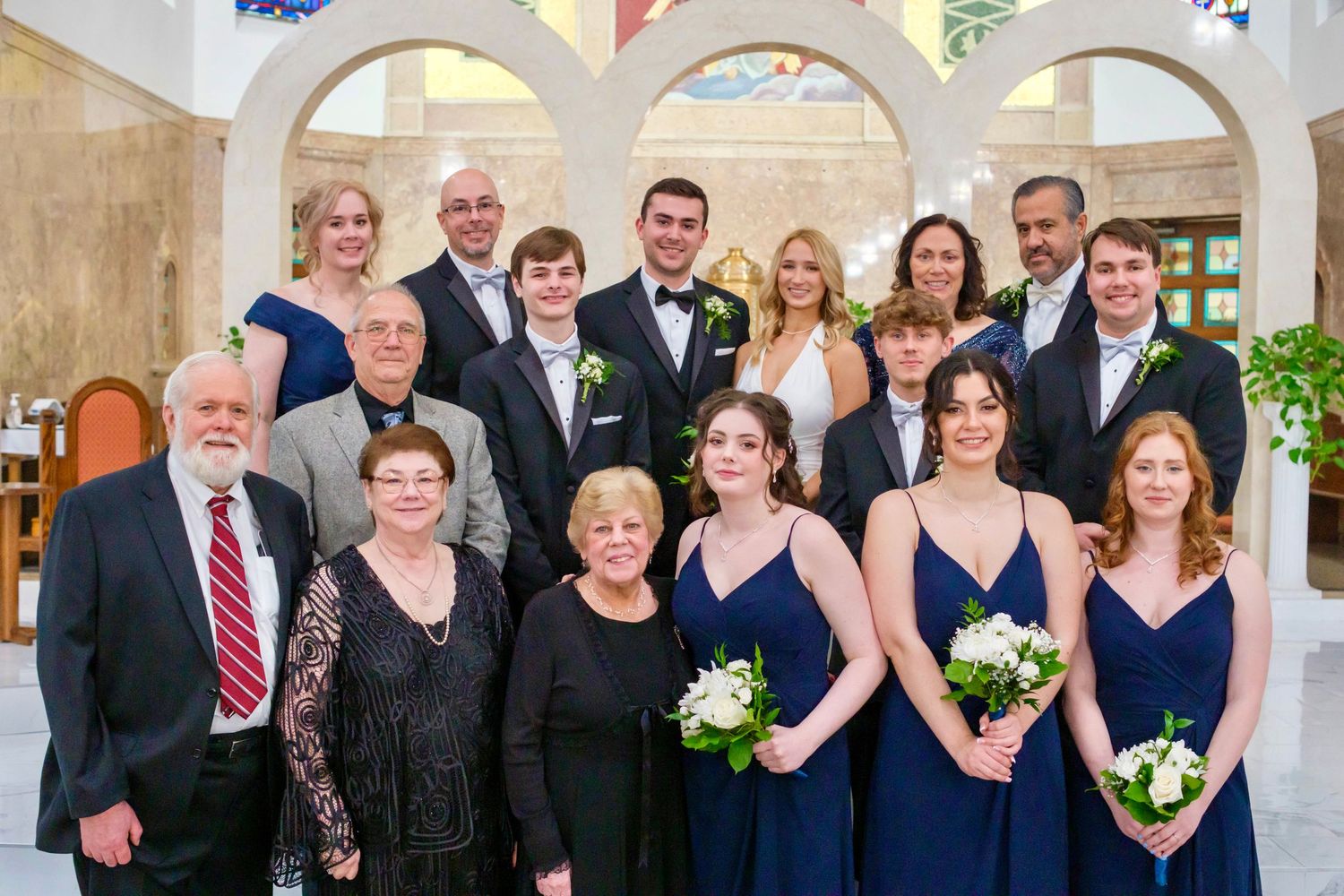 Large family group portrait at an elegant wedding venue with arched doorways and floral decor.