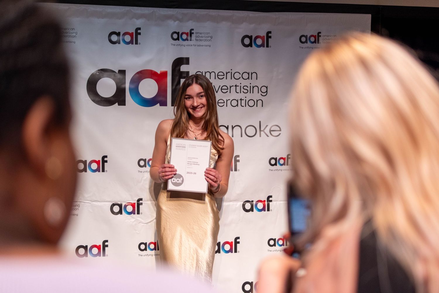 Young woman smiles holding certificate at AAF American Advertising Federation awards event.