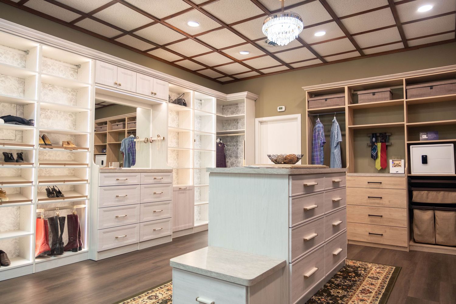 Luxury walk-in closet with white built-in shelving, center island with drawers, coffered ceiling, and hardwood floors.
