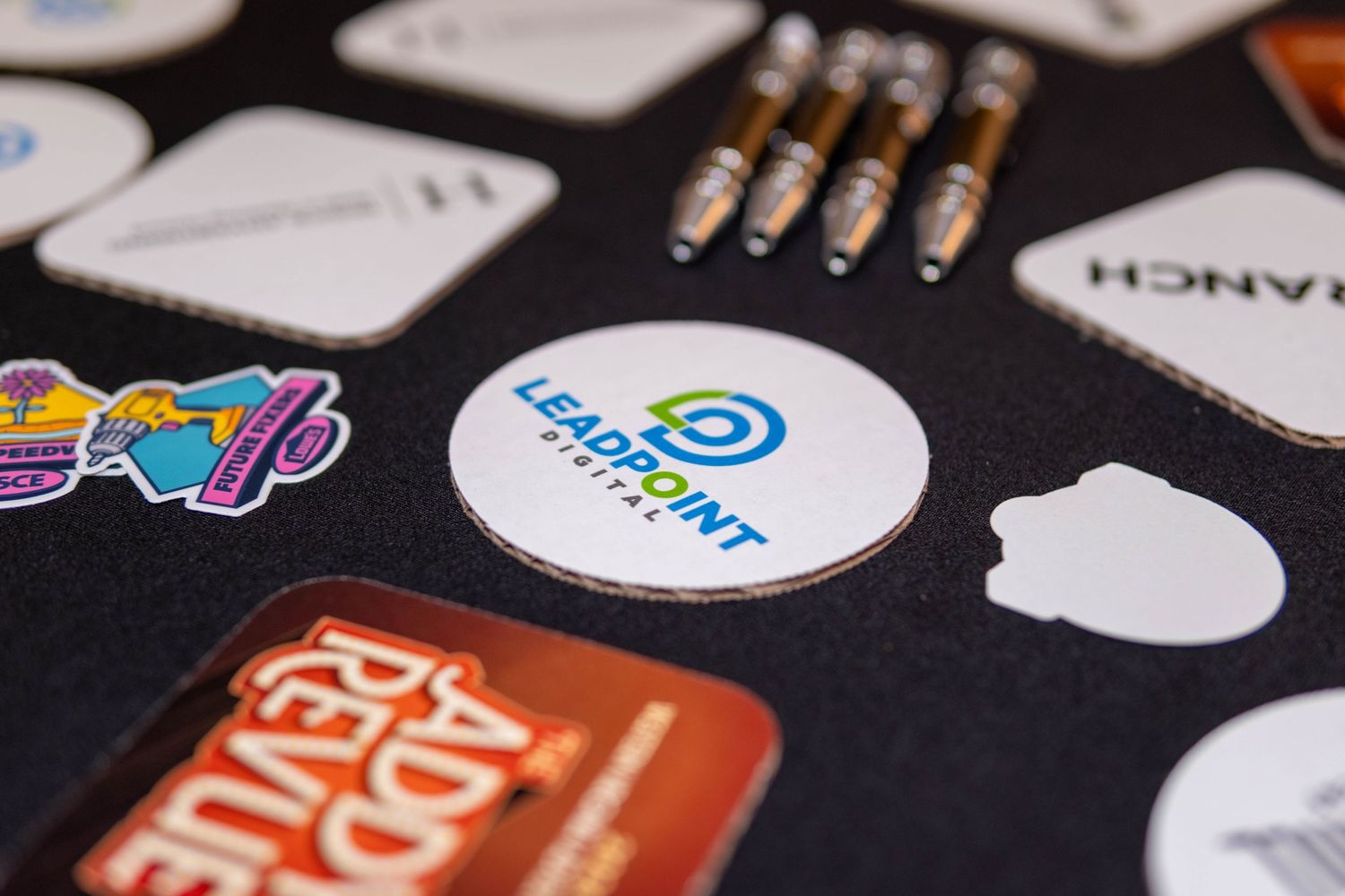 Leadpoint Digital branded sticker displayed among various company stickers and pens on dark surface.