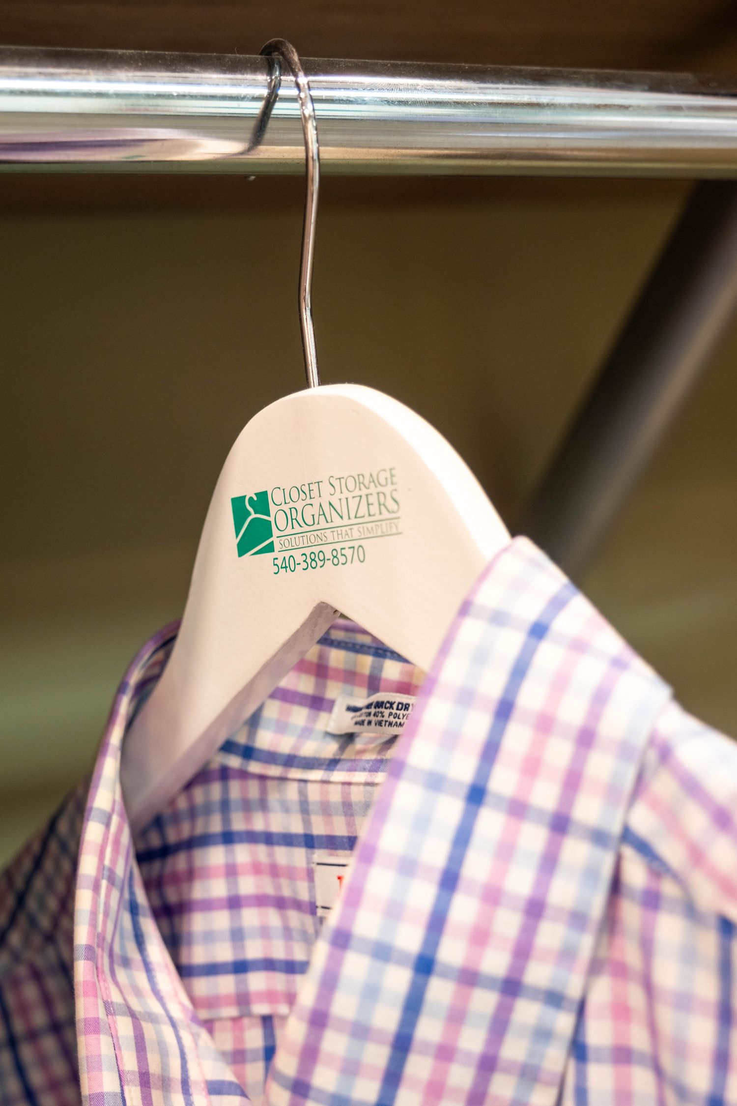 A plaid shirt hanging on a branded Closet Storage Organizers hanger on a metal rod.