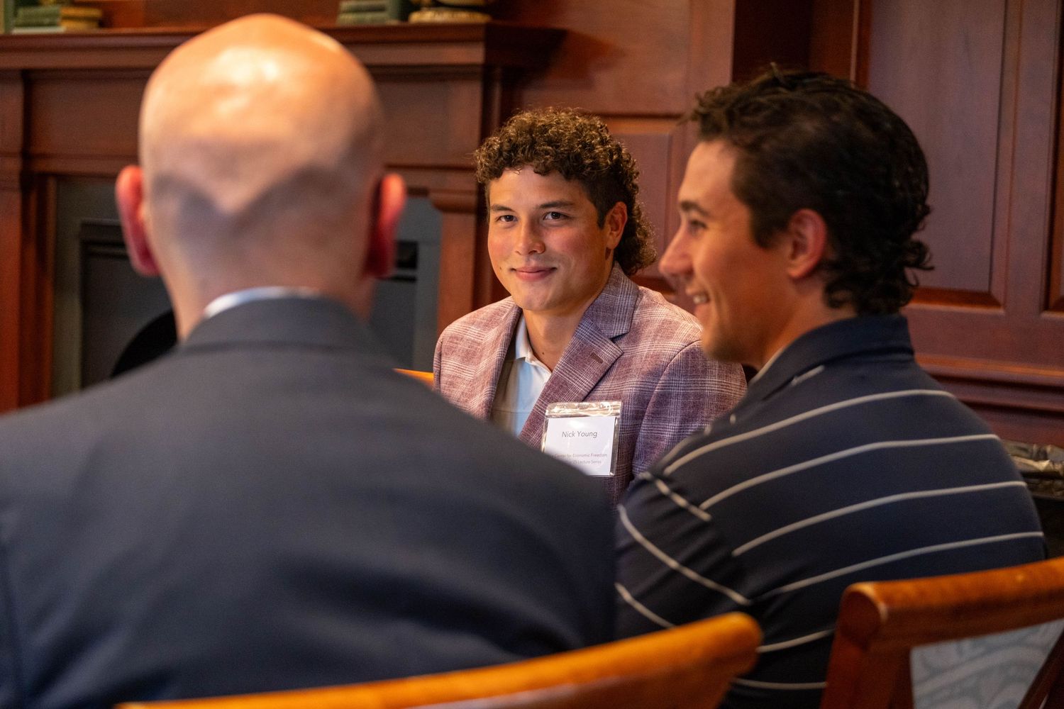 Three professional men in business attire engage in conversation at a formal networking event indoors.