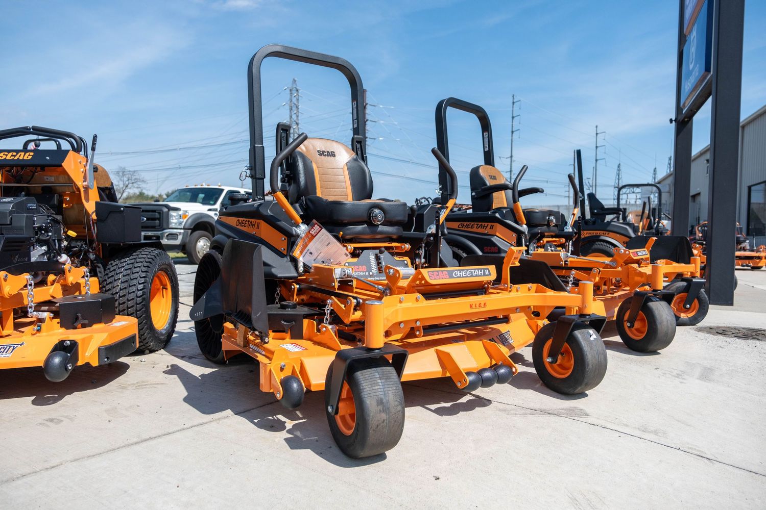 Orange SCAG zero-turn commercial lawn mowers lined up outside a dealership on a sunny day.