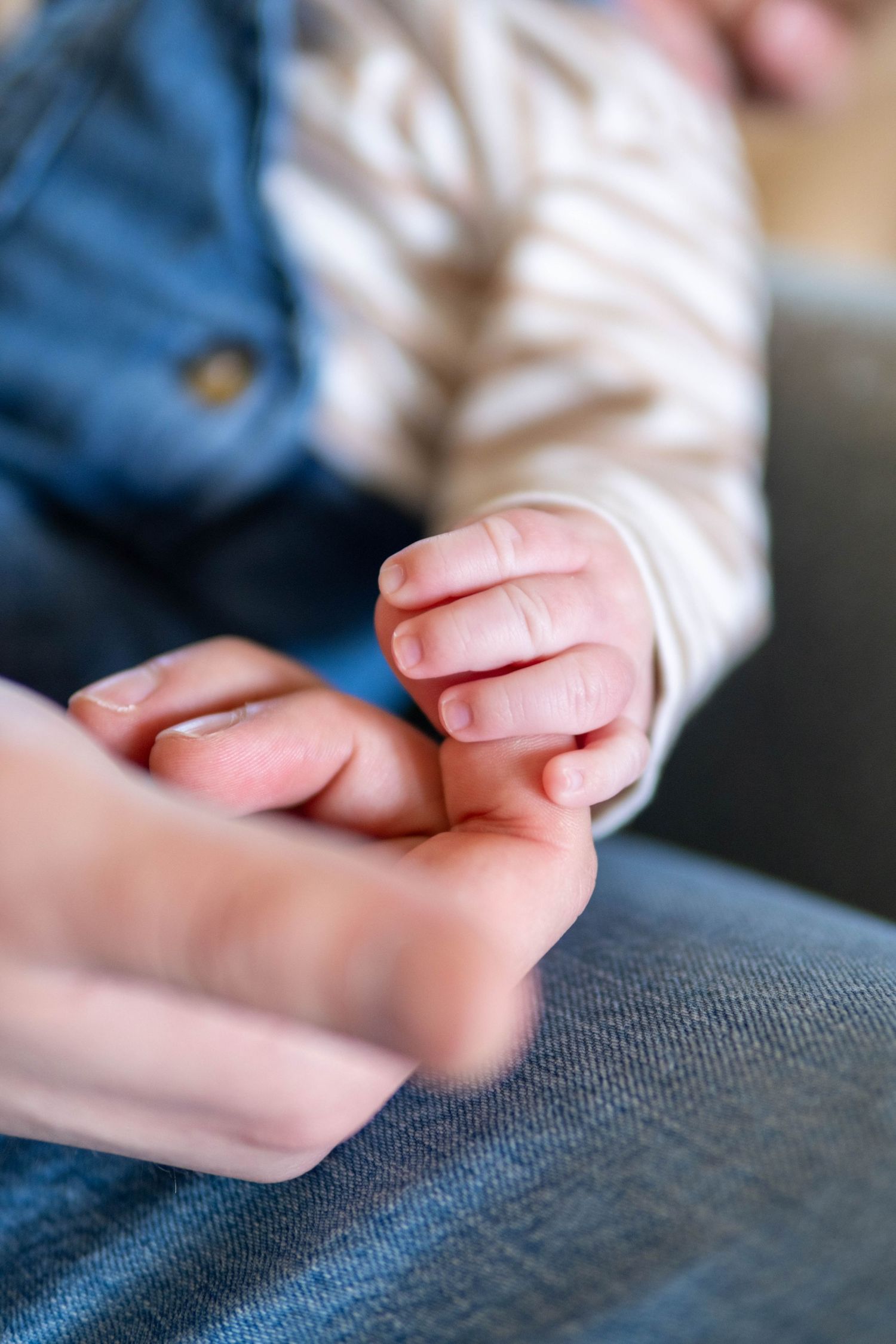 Close-up of adult gently holding tiny newborn baby hand indoors.