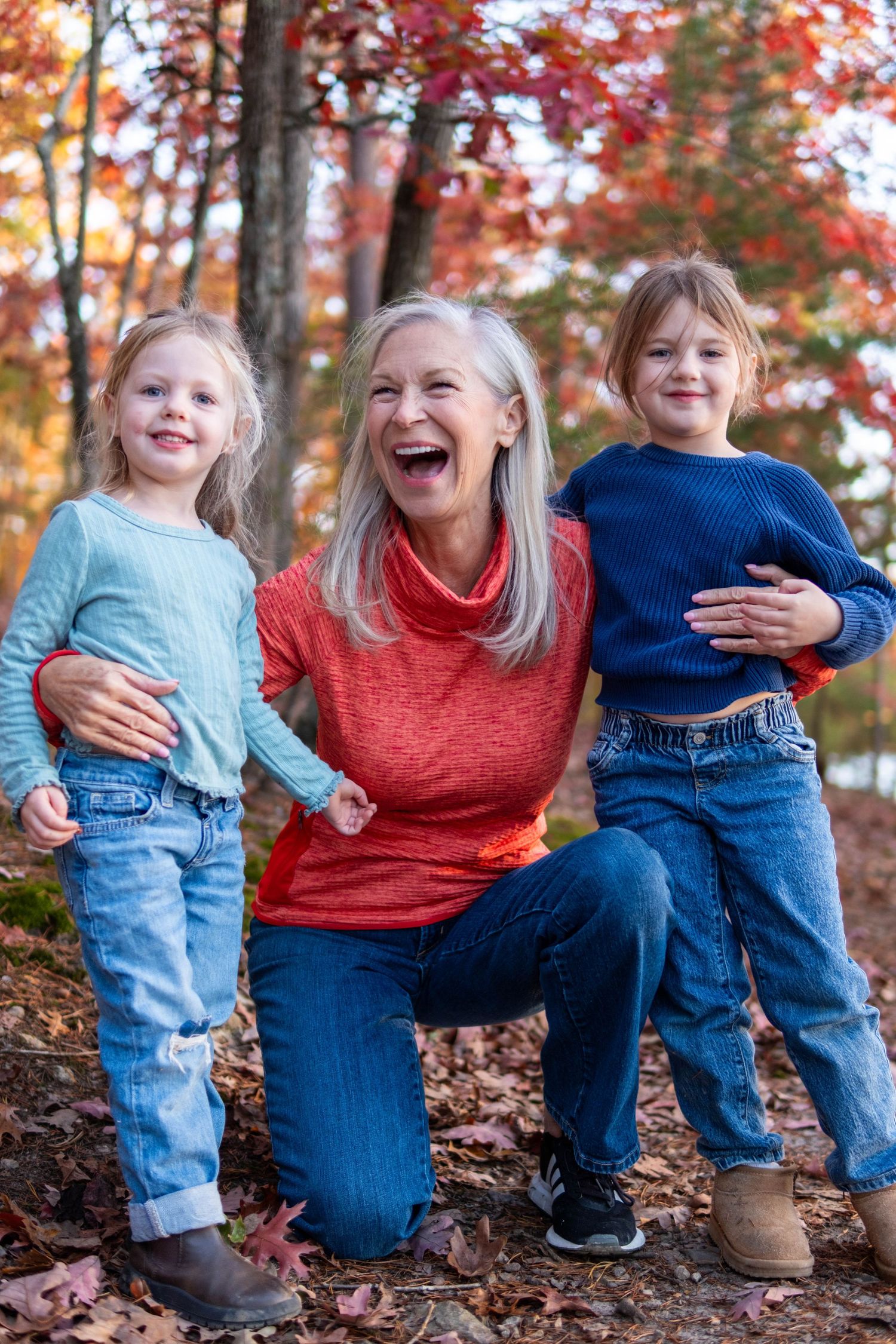Grandmother laughing joyfully with two young grandchildren in autumn forest setting.