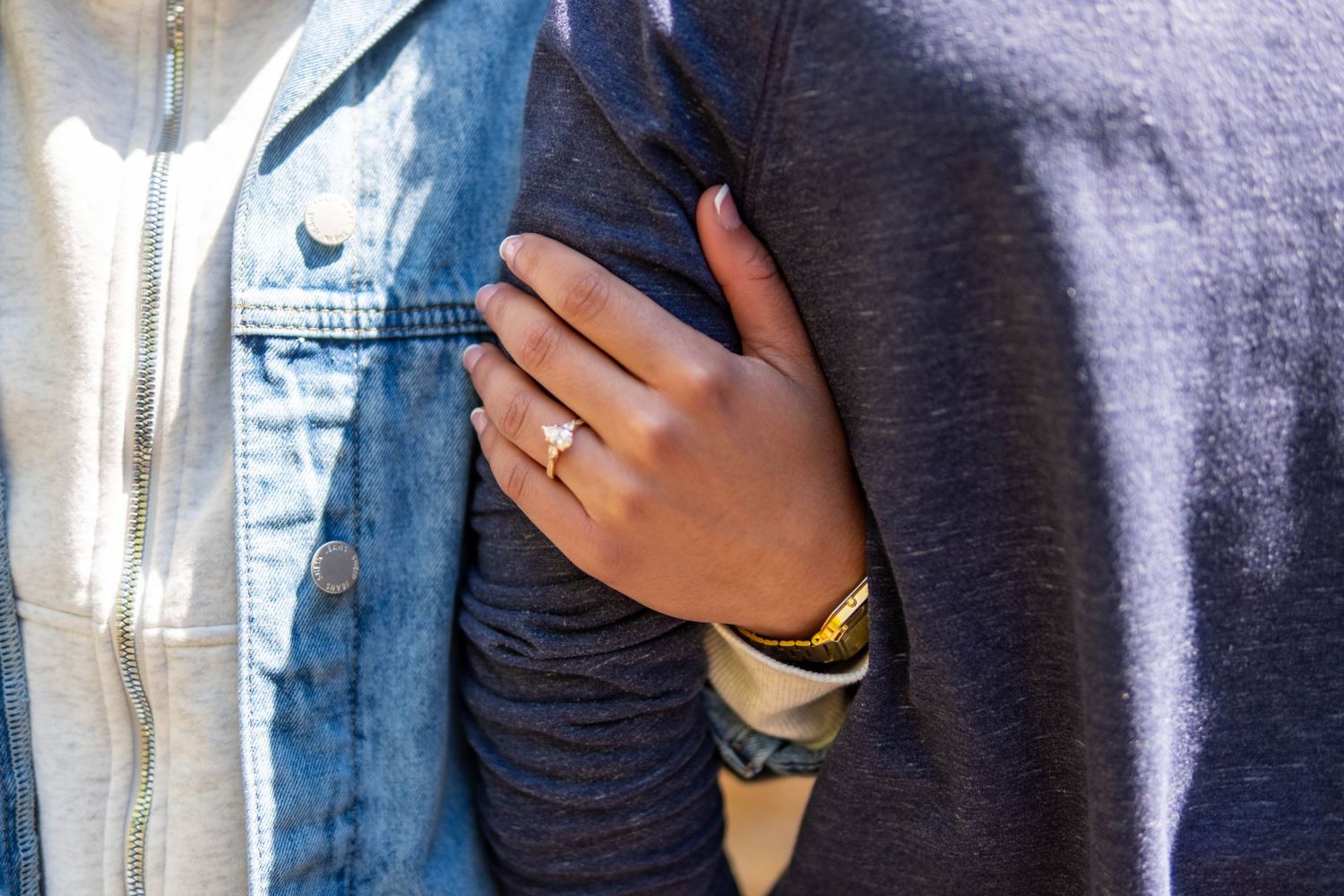 Close-up of a woman's hand with a gold ring resting on a man's chest, wearing denim and gray shirts.