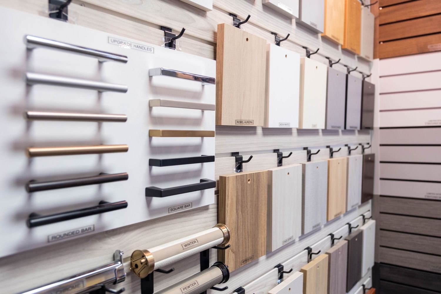 Display wall of cabinet door samples and handle options in various wood finishes at a kitchen showroom.