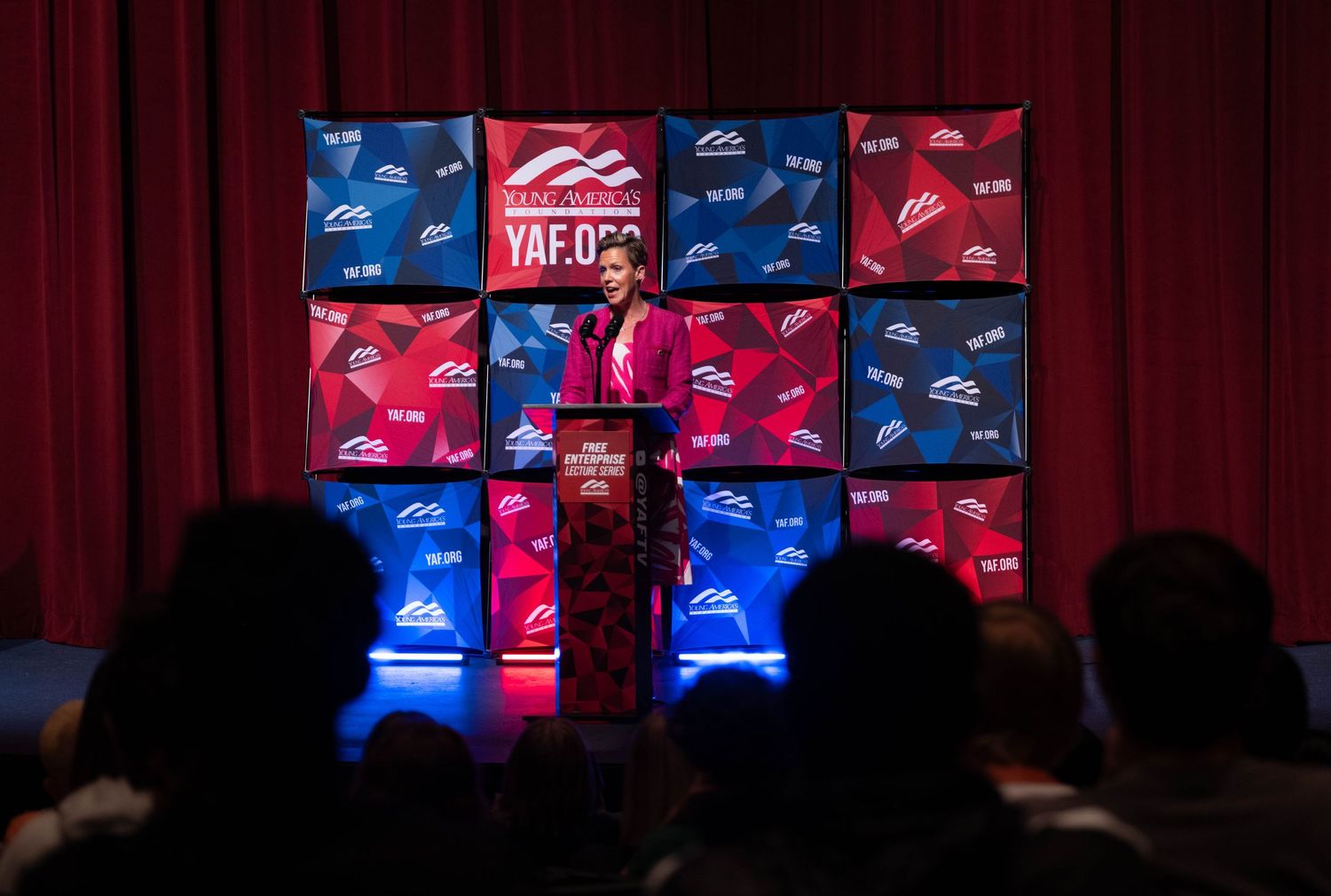 Speaker at podium presenting at YAF.org conservative youth conference on red curtain stage.