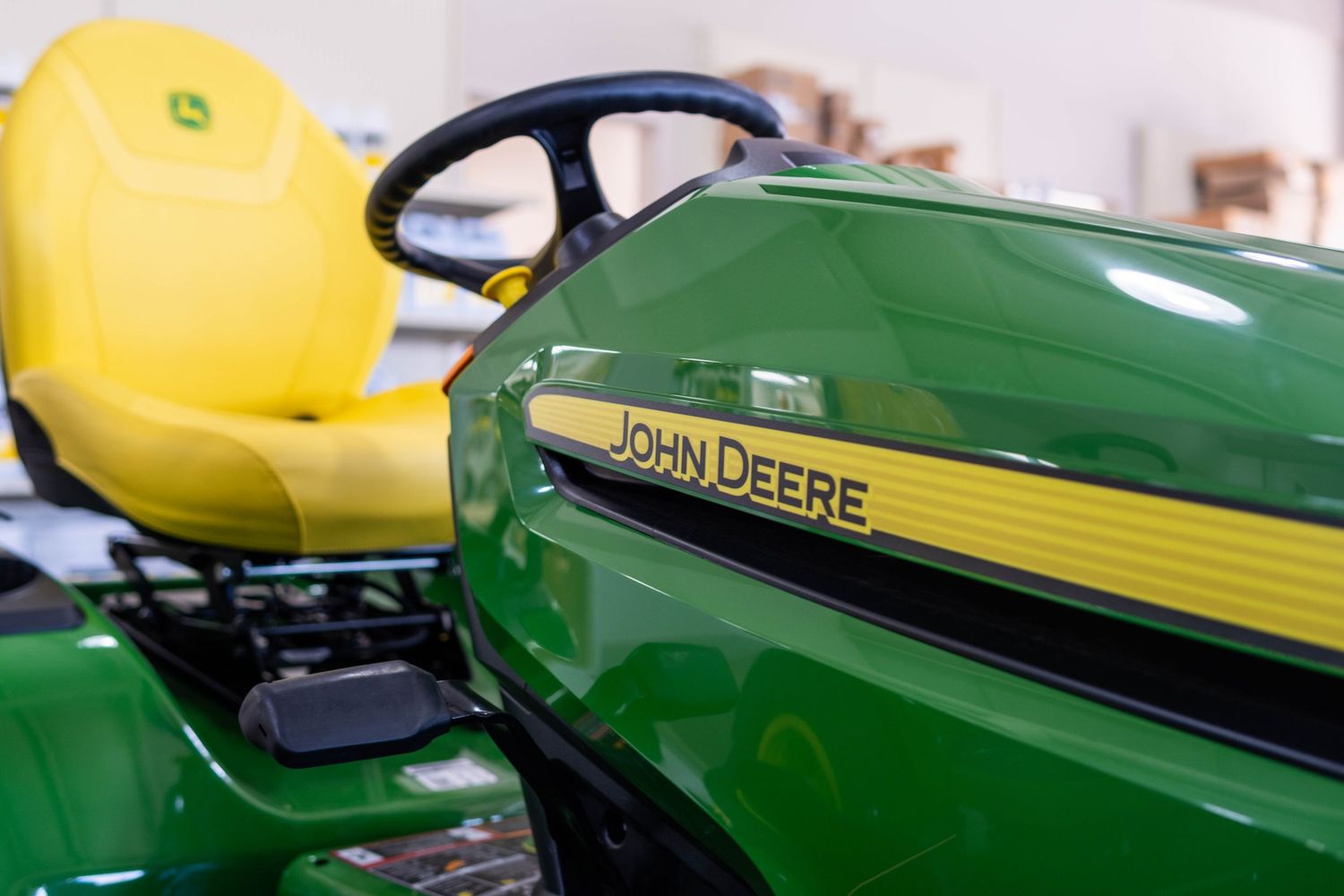Close-up of a John Deere riding lawn mower showing the brand logo and yellow seat.